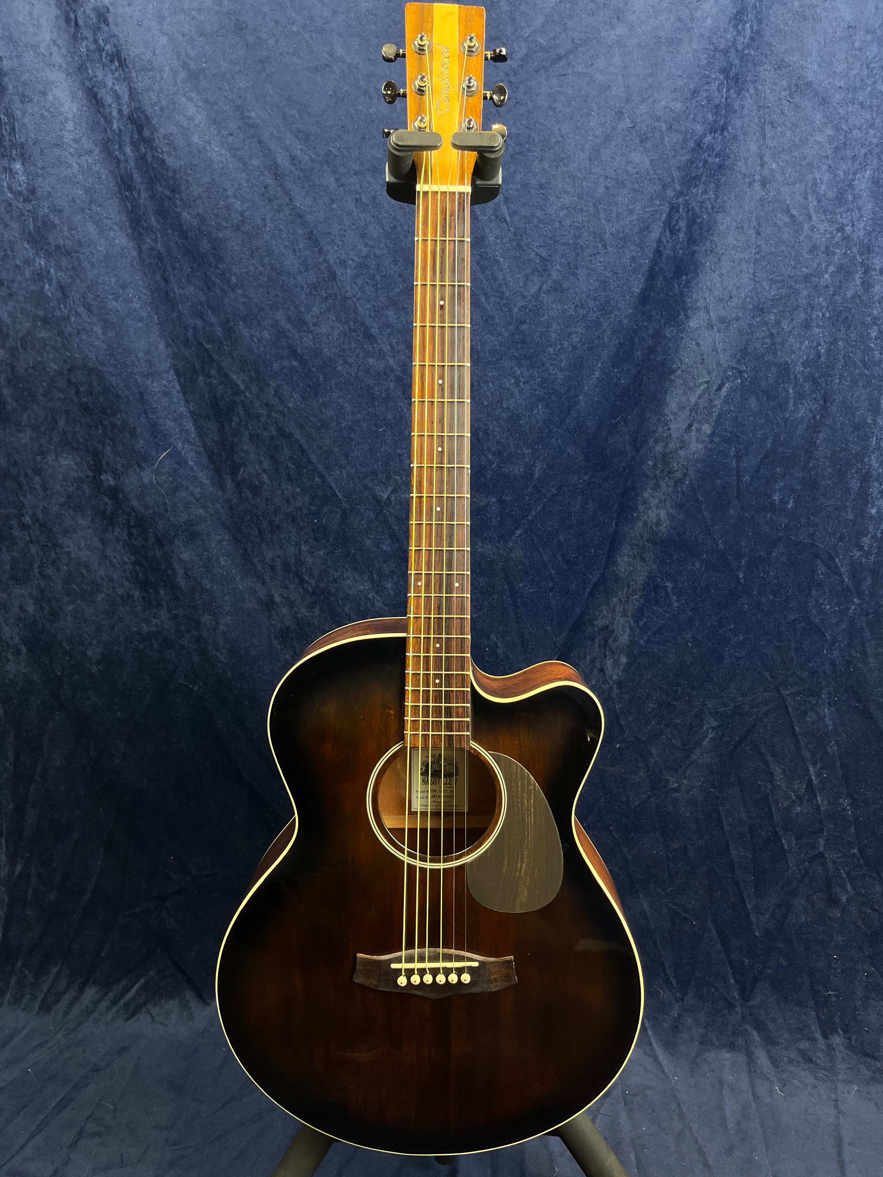 Dark brown acoustic guitar with a cutaway body shape, six strings, light wooden neck, and circular sound hole, set against a dark blue background.