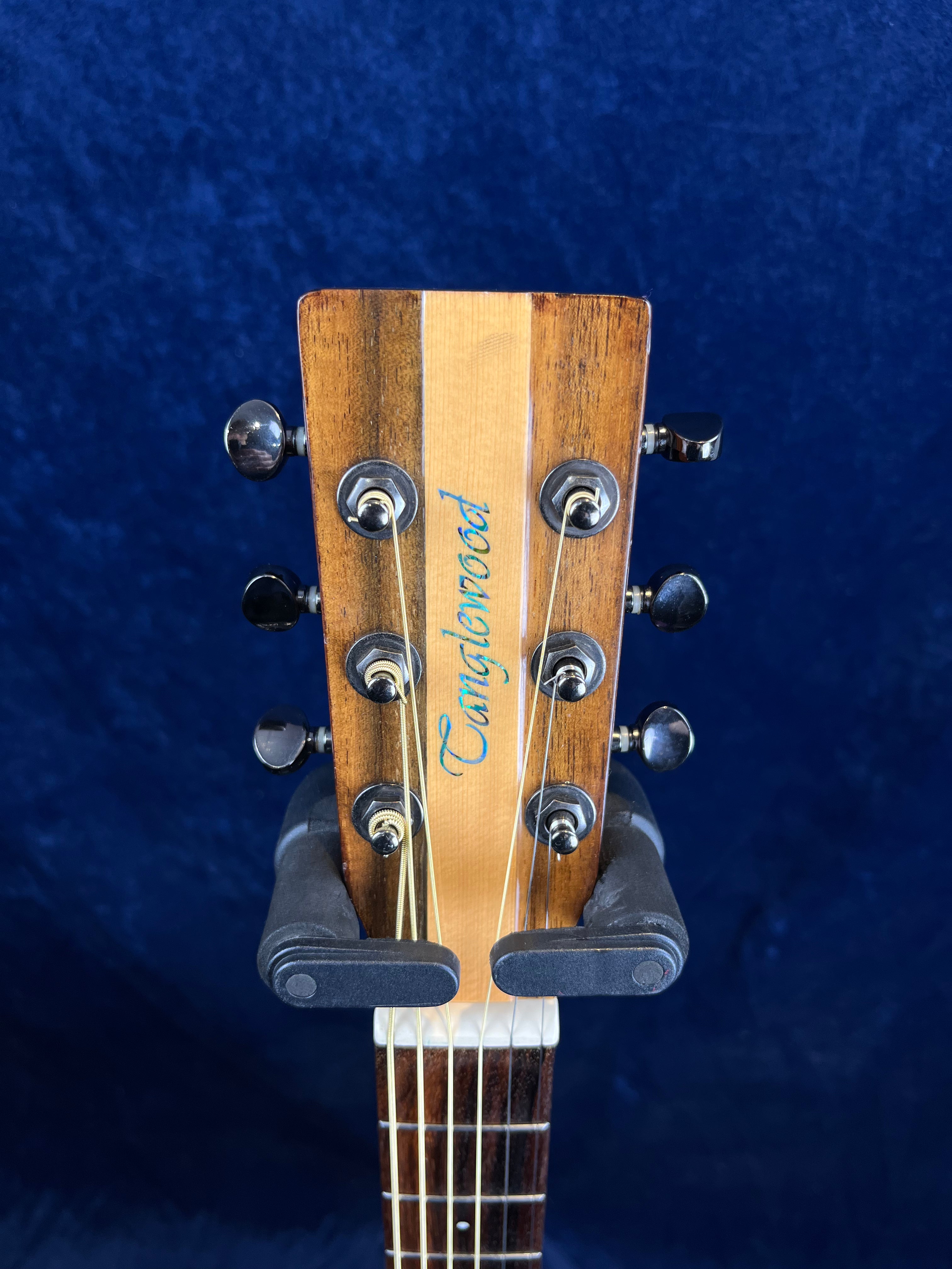 Close-up of an acoustic guitar headstock with six tuning pegs, wood grain finish, and "Tanglewood" logo in blue script.