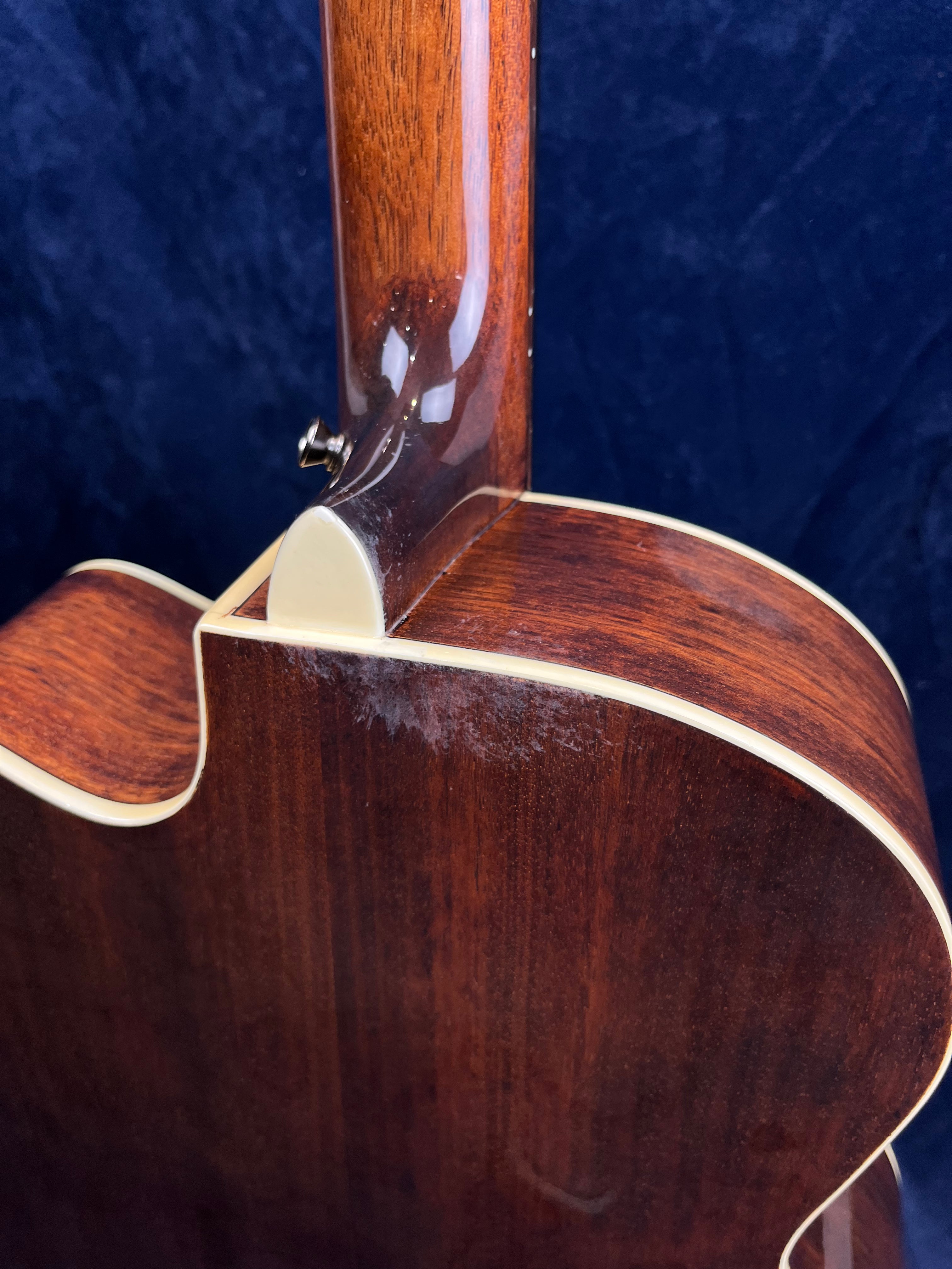 Glossy brown acoustic guitar back and neck joint with cream binding; visible white scuff marks near the neck heel on the body.
