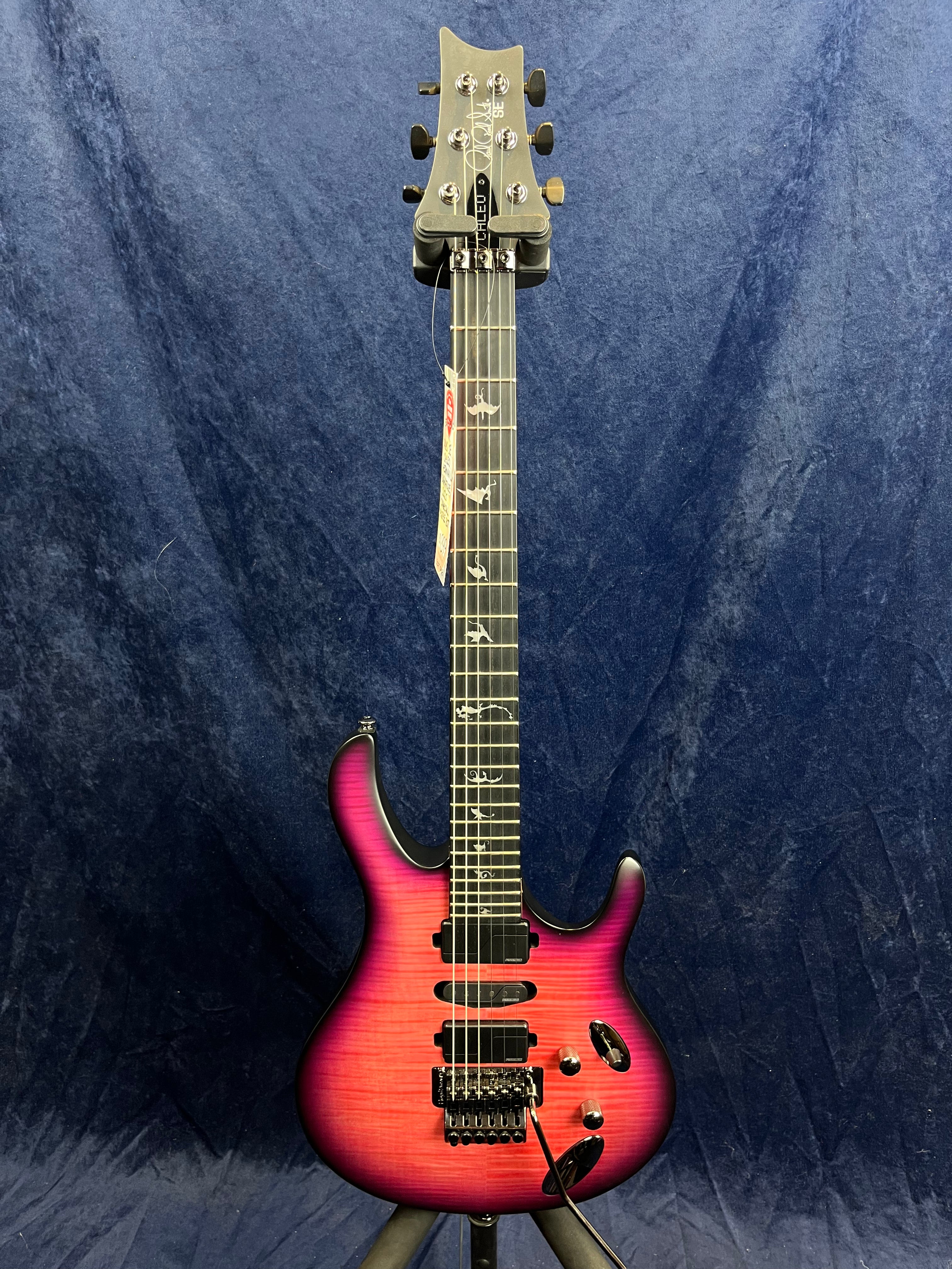 Electric guitar with a vibrant pink-to-purple gradient body, black hardware, three pickups, and distinctive bird inlays on the fretboard.