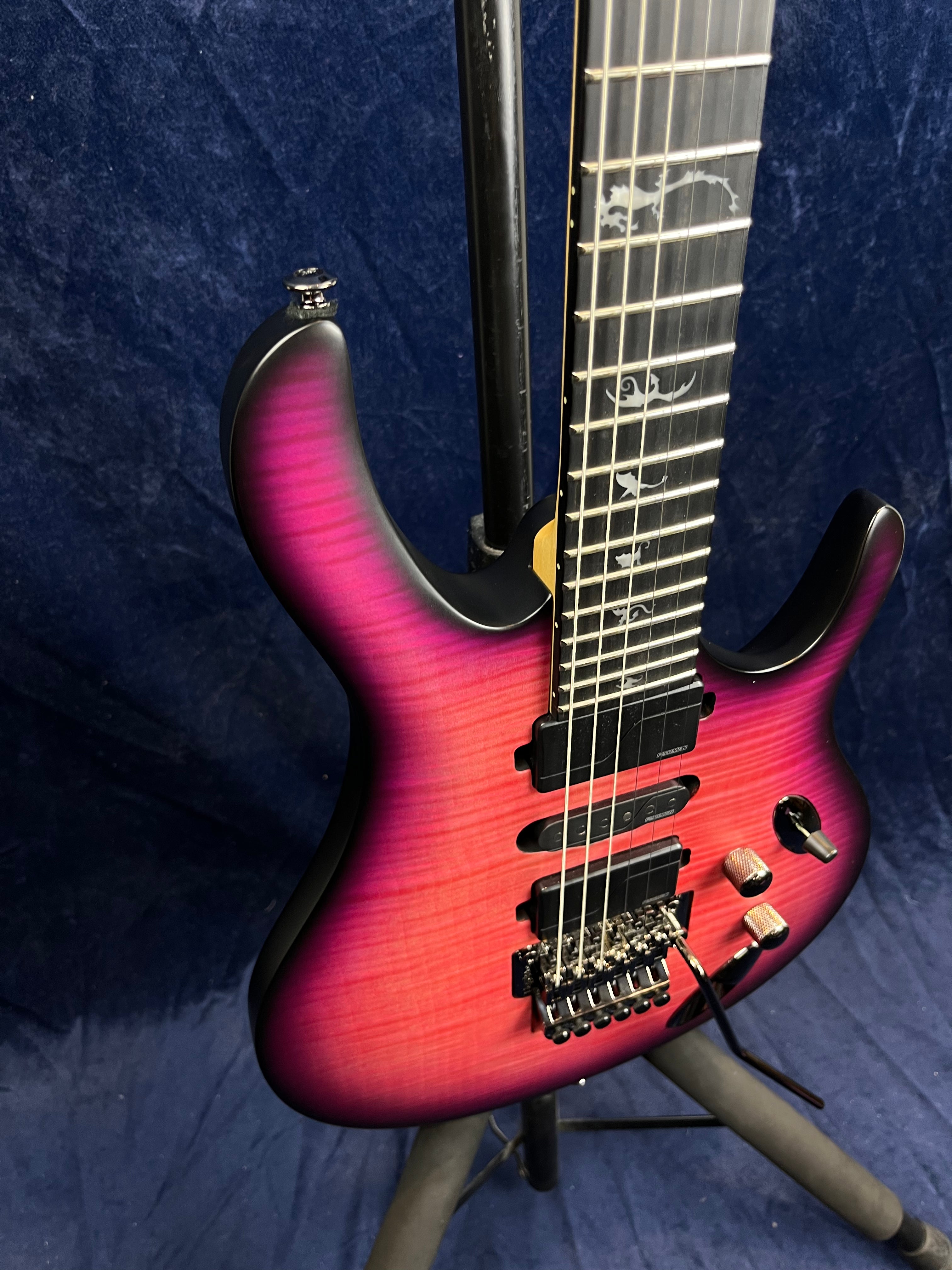 Electric guitar with a pink-to-purple gradient finish, three pickups, decorative fret inlays, metallic knobs, and a tremolo bridge.