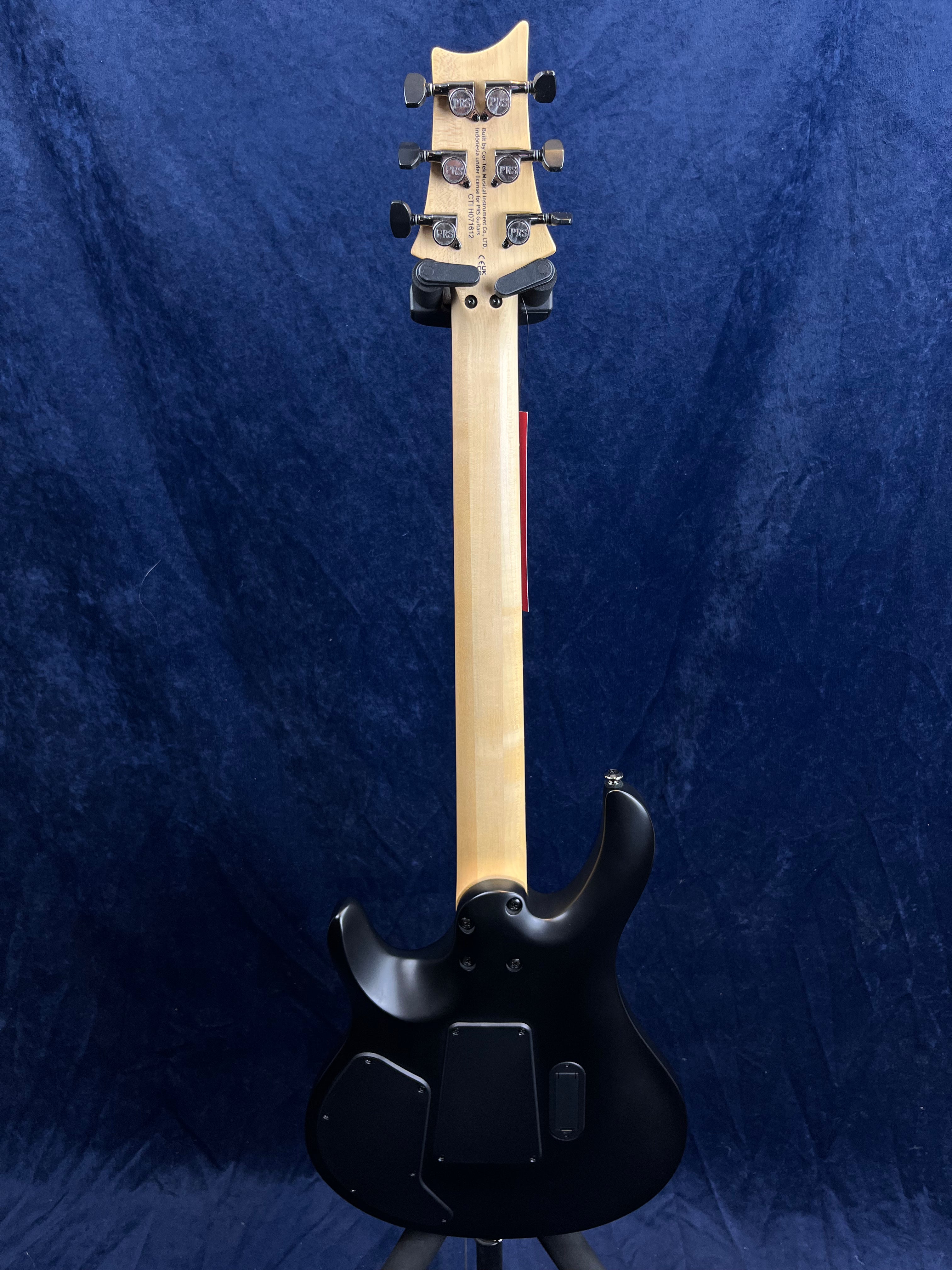 Electric guitar shown from the back with a natural wood neck, black body, and six tuning pegs; two access panels on the body.