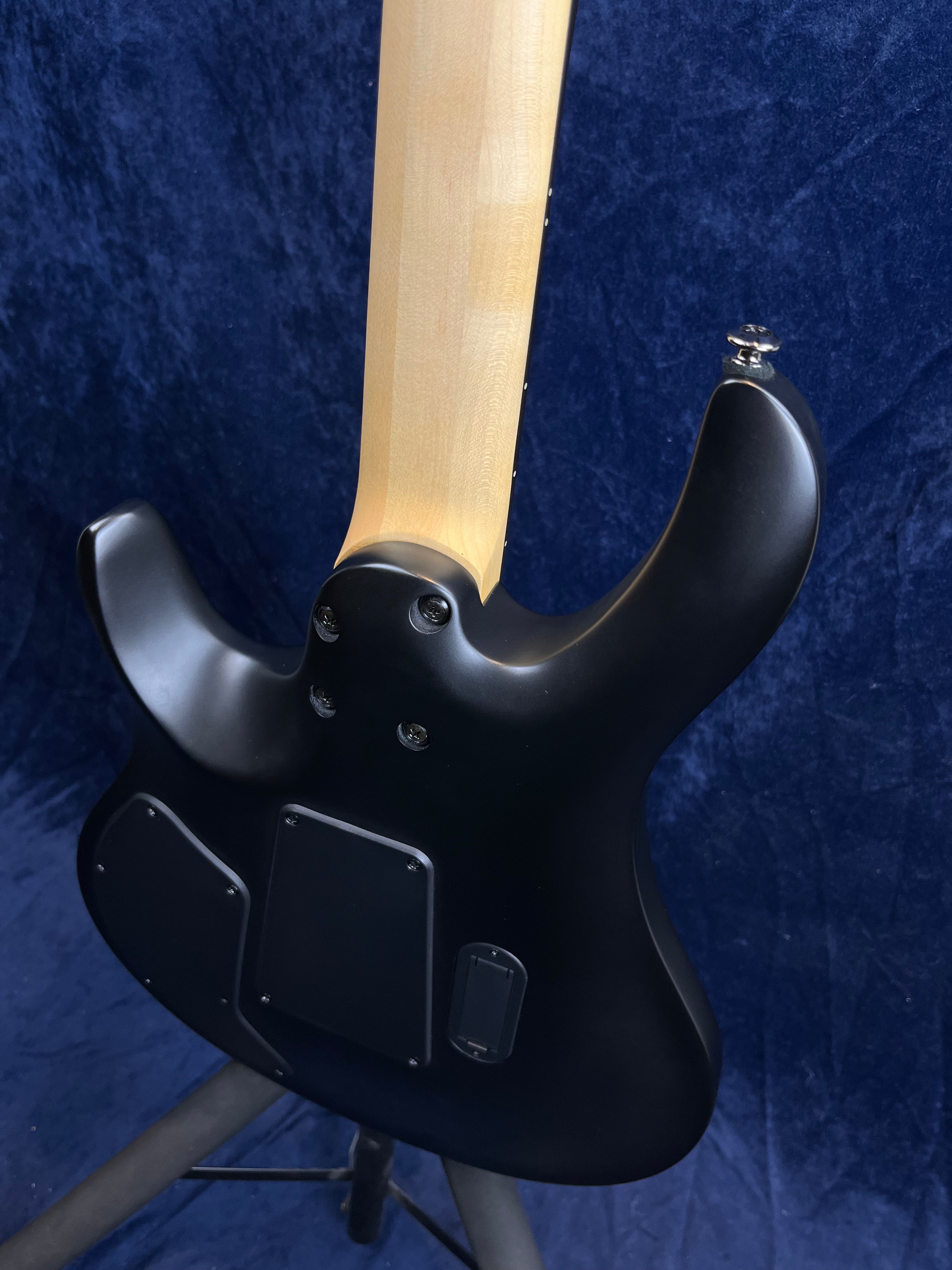 Matte black electric guitar shown from the back, revealing its natural wood neck and several electronic access panels on the body.