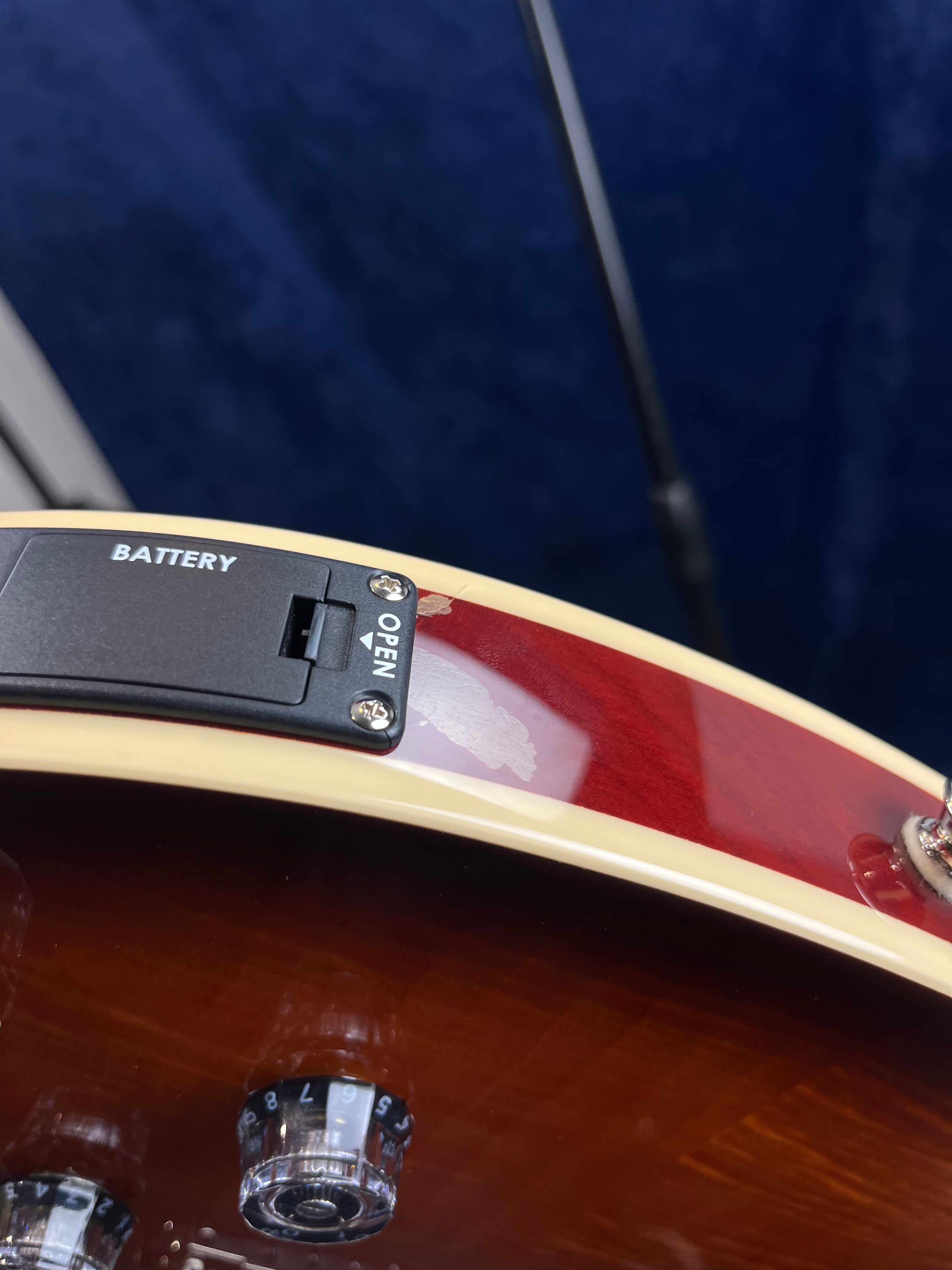 Electric guitar body with a battery compartment, cream edge binding, and visible paint damage or chip near the compartment. Two control knobs visible below.
