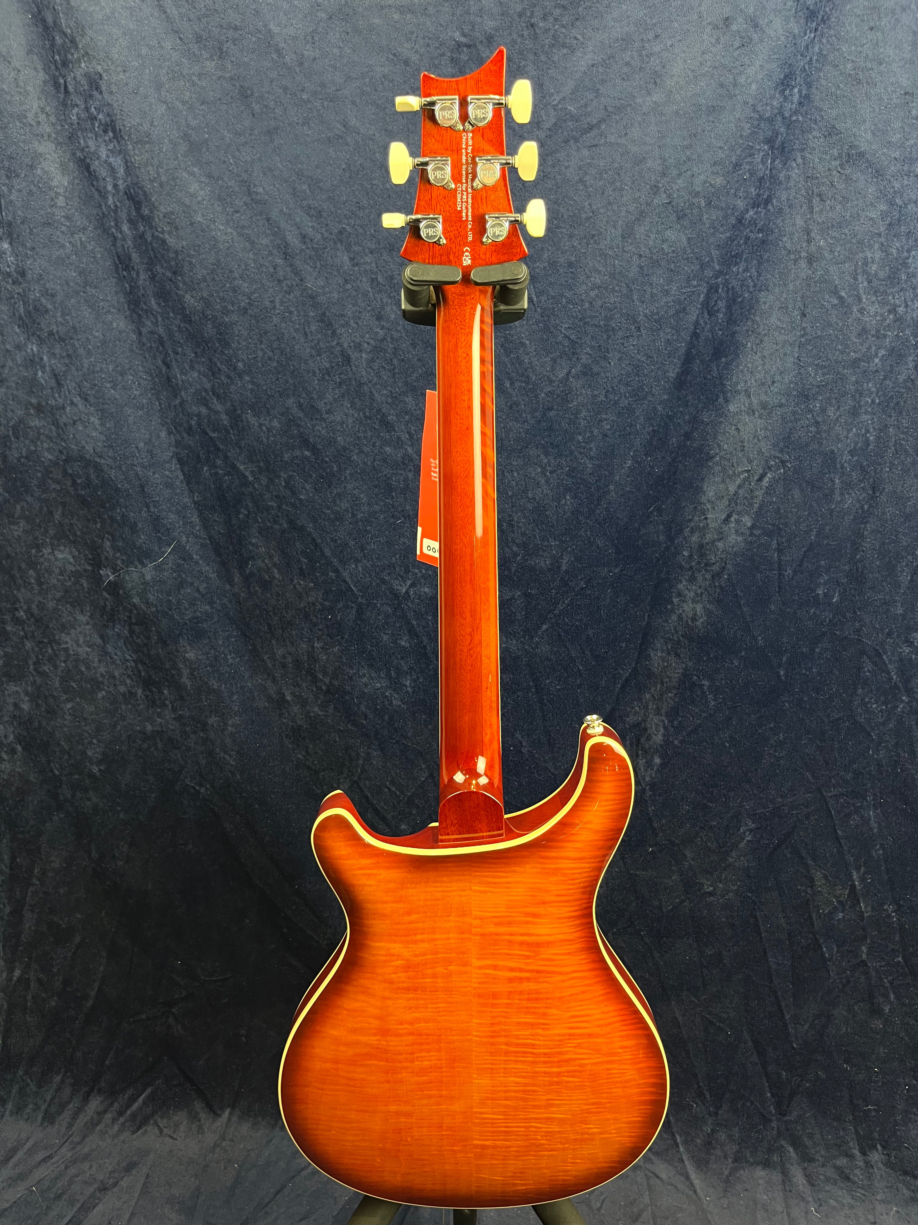 Sunburst-finish electric guitar seen from the back, showing a contoured body with cream binding, six tuning pegs, and a glossy red neck.