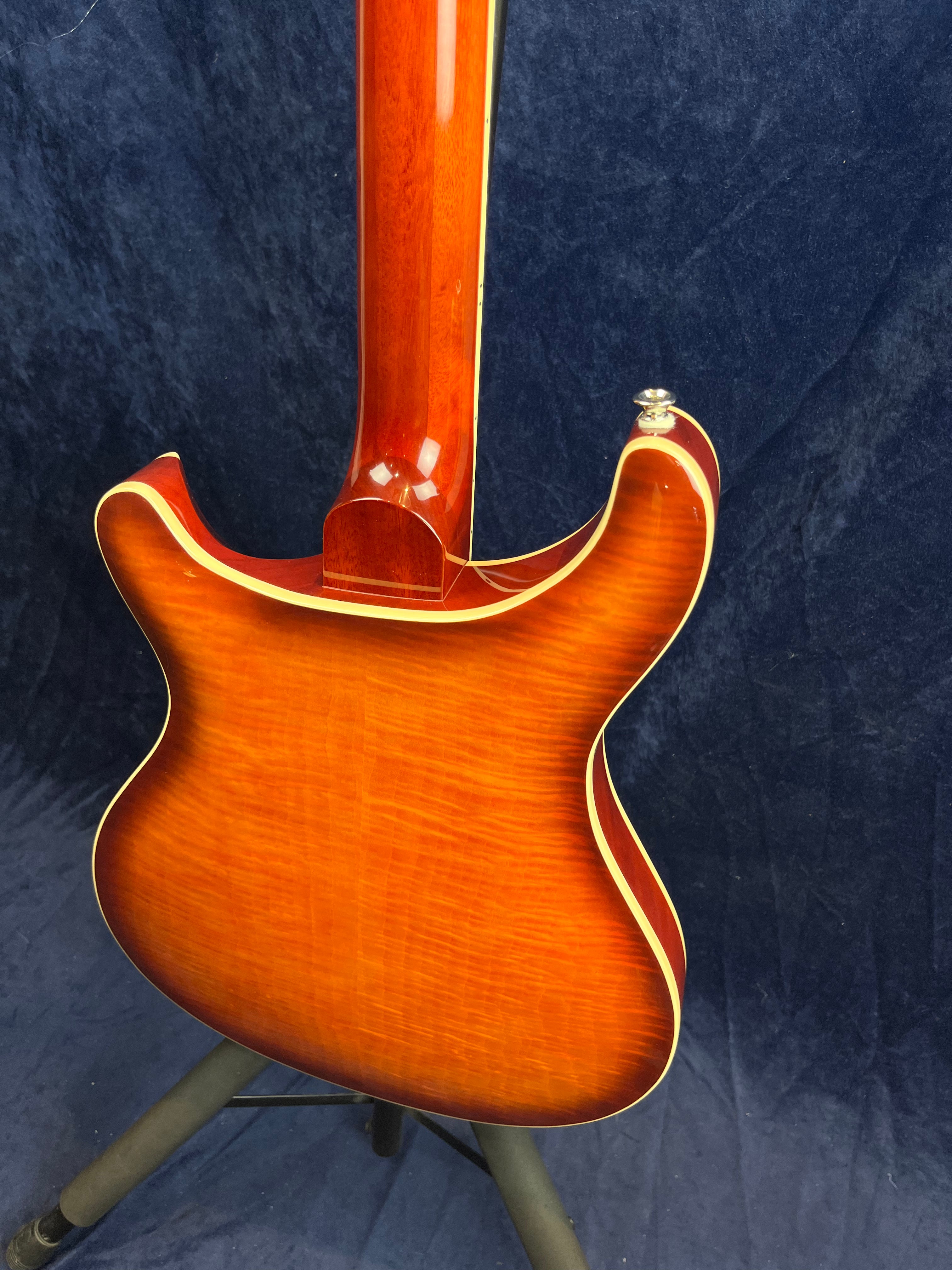 Electric guitar with a glossy sunburst finish, cream binding accents, and visible wood grain on the back; shown upright on a stand.