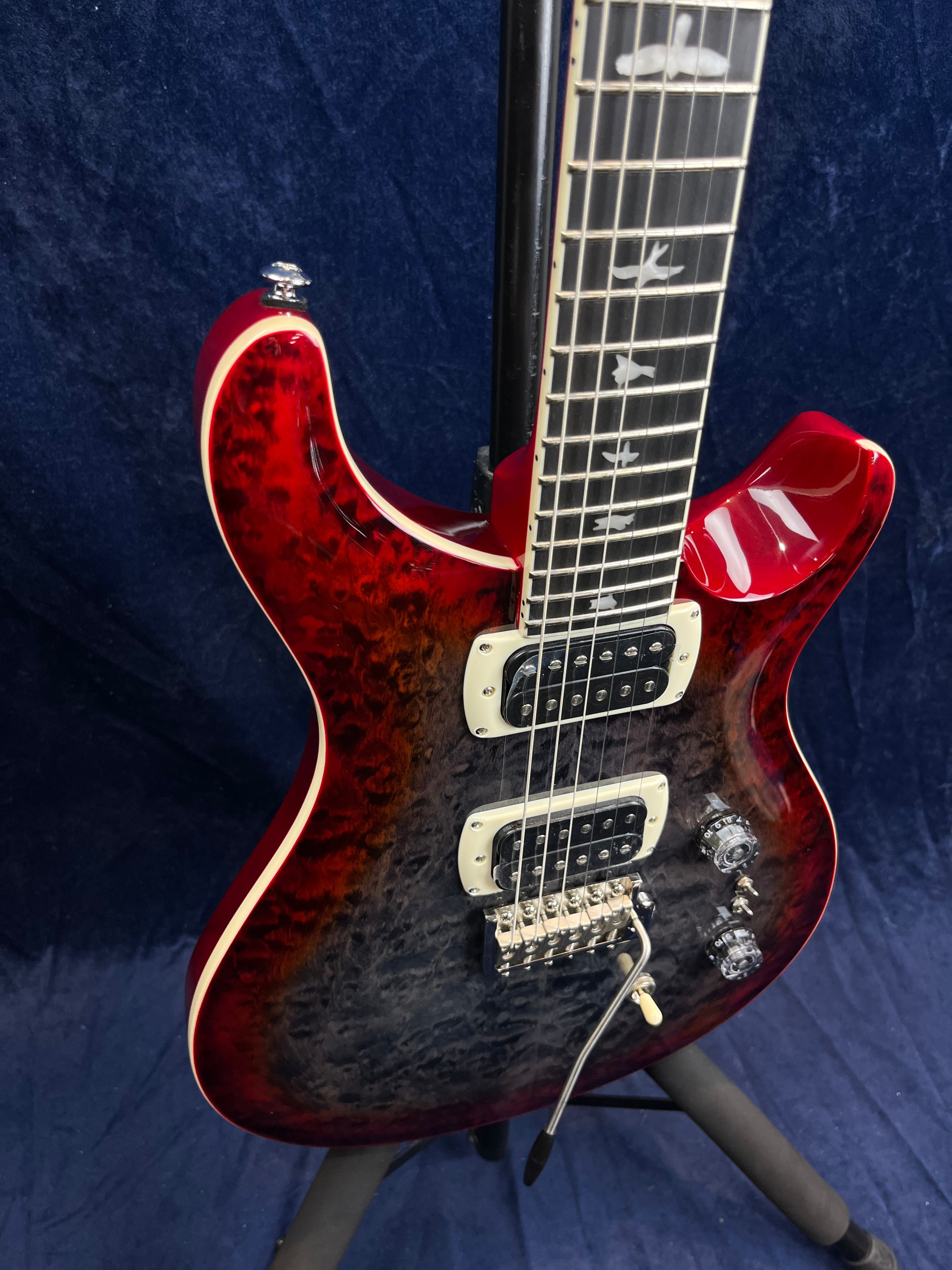 Electric guitar with a quilted dark red and black body, two humbucker pickups, bird inlays on the fretboard, chrome hardware, and whammy bar.