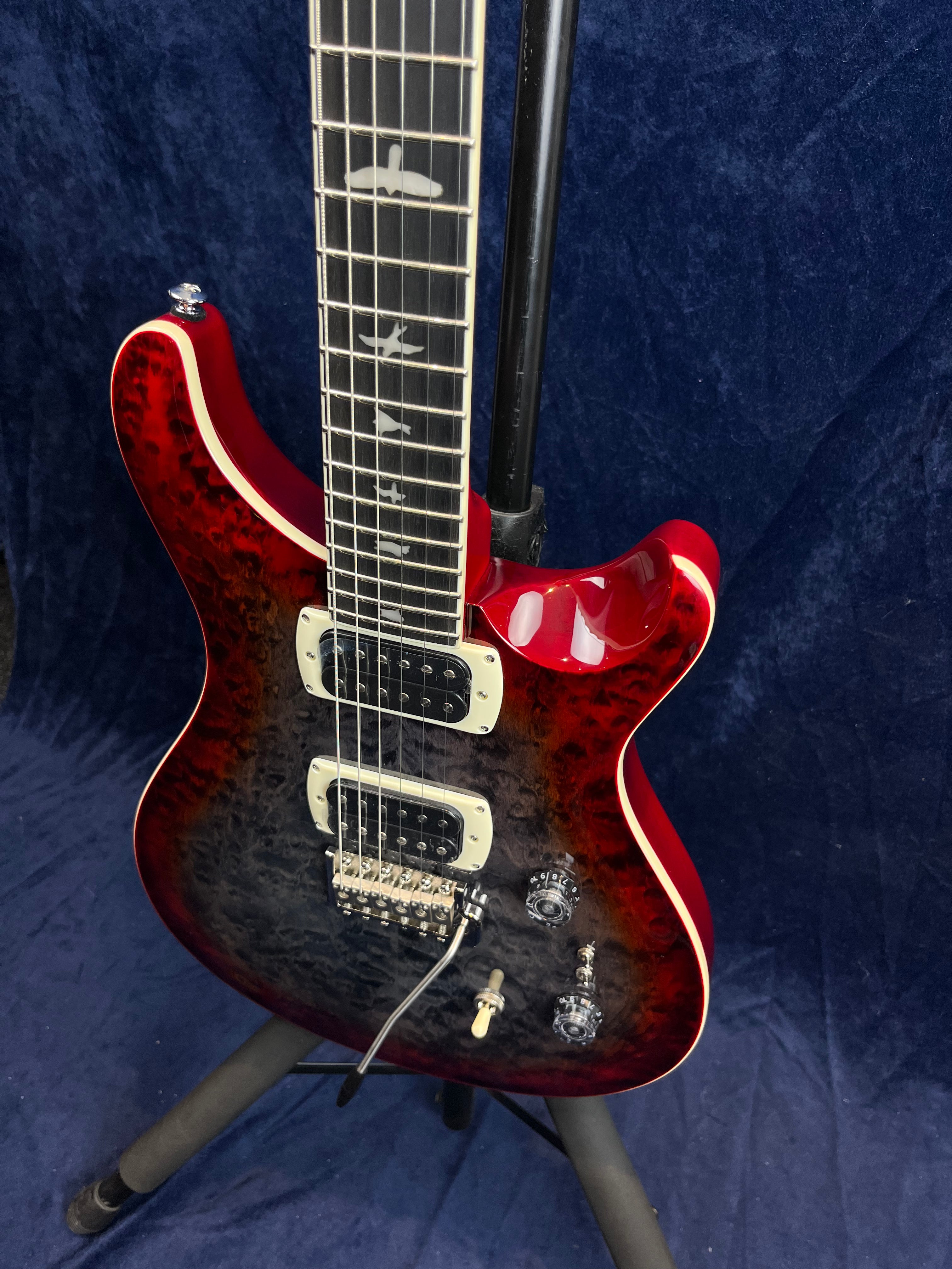 Red electric guitar with a quilted black burst finish, two humbucker pickups, bird inlays on the fretboard, and chrome control knobs.