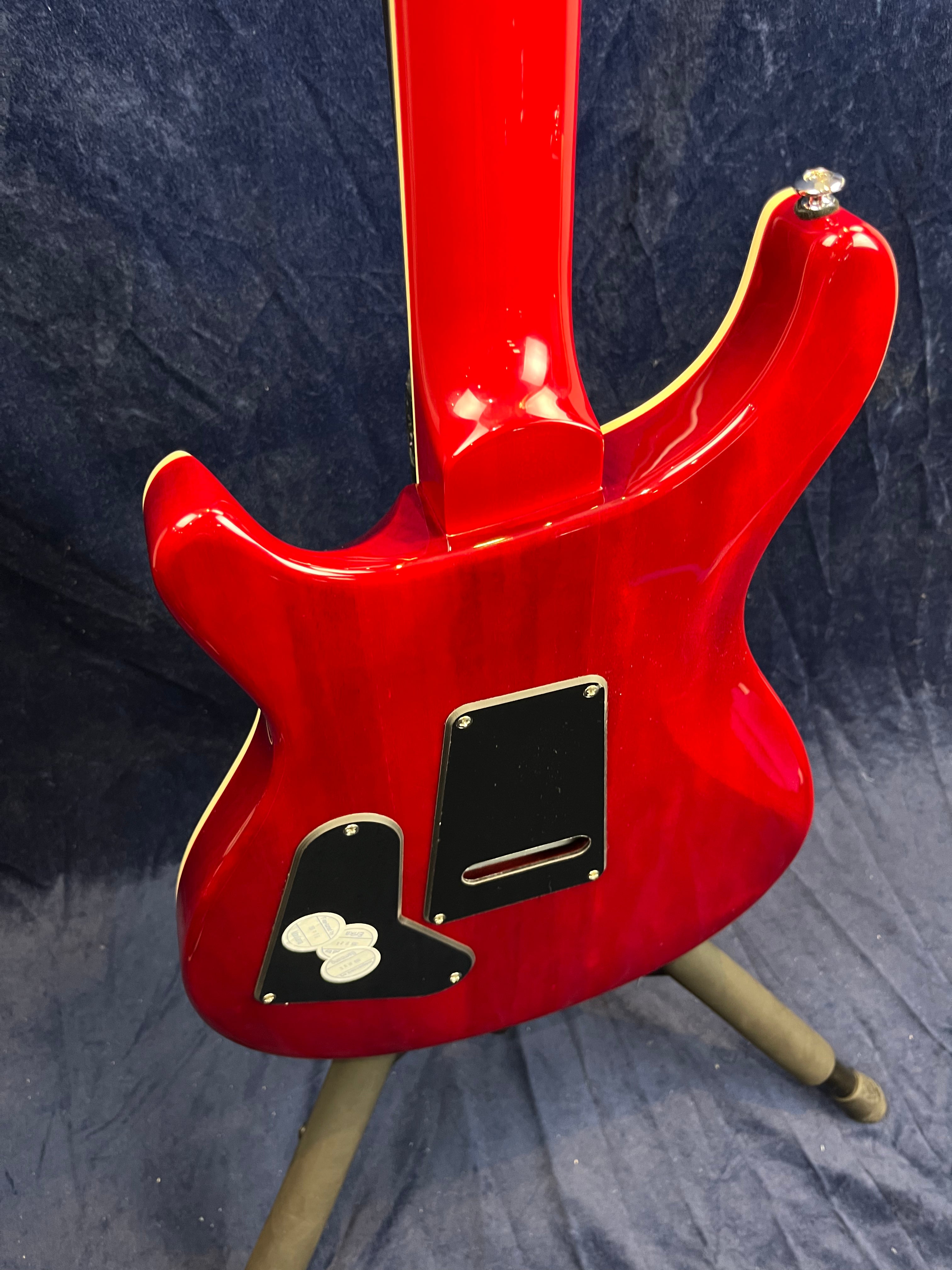 Red electric guitar shown from the back, with black access plates and three white guitar picks resting on one of the plates.