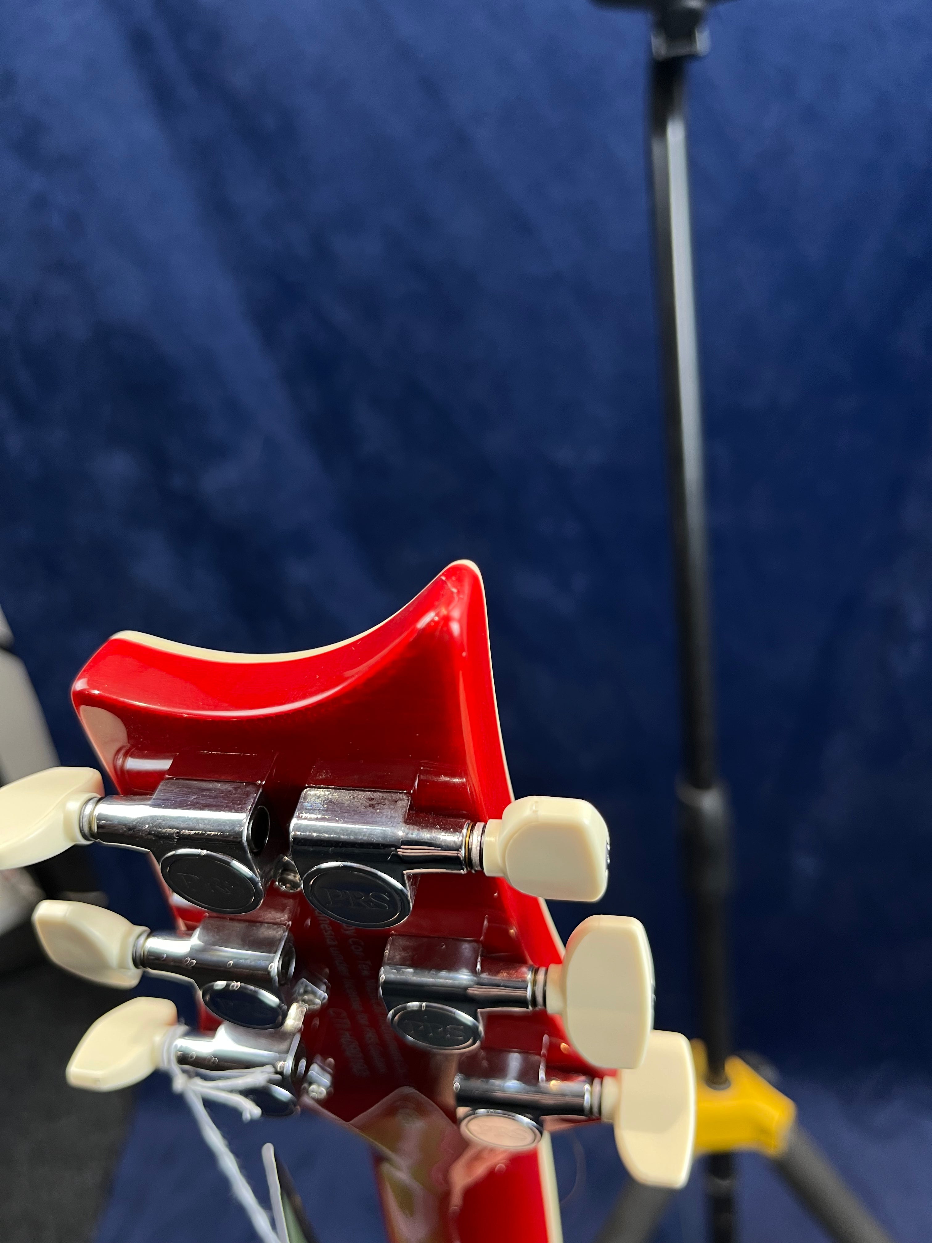 Red electric guitar headstock with six silver tuning pegs and cream-colored knobs, set against a dark blue background.