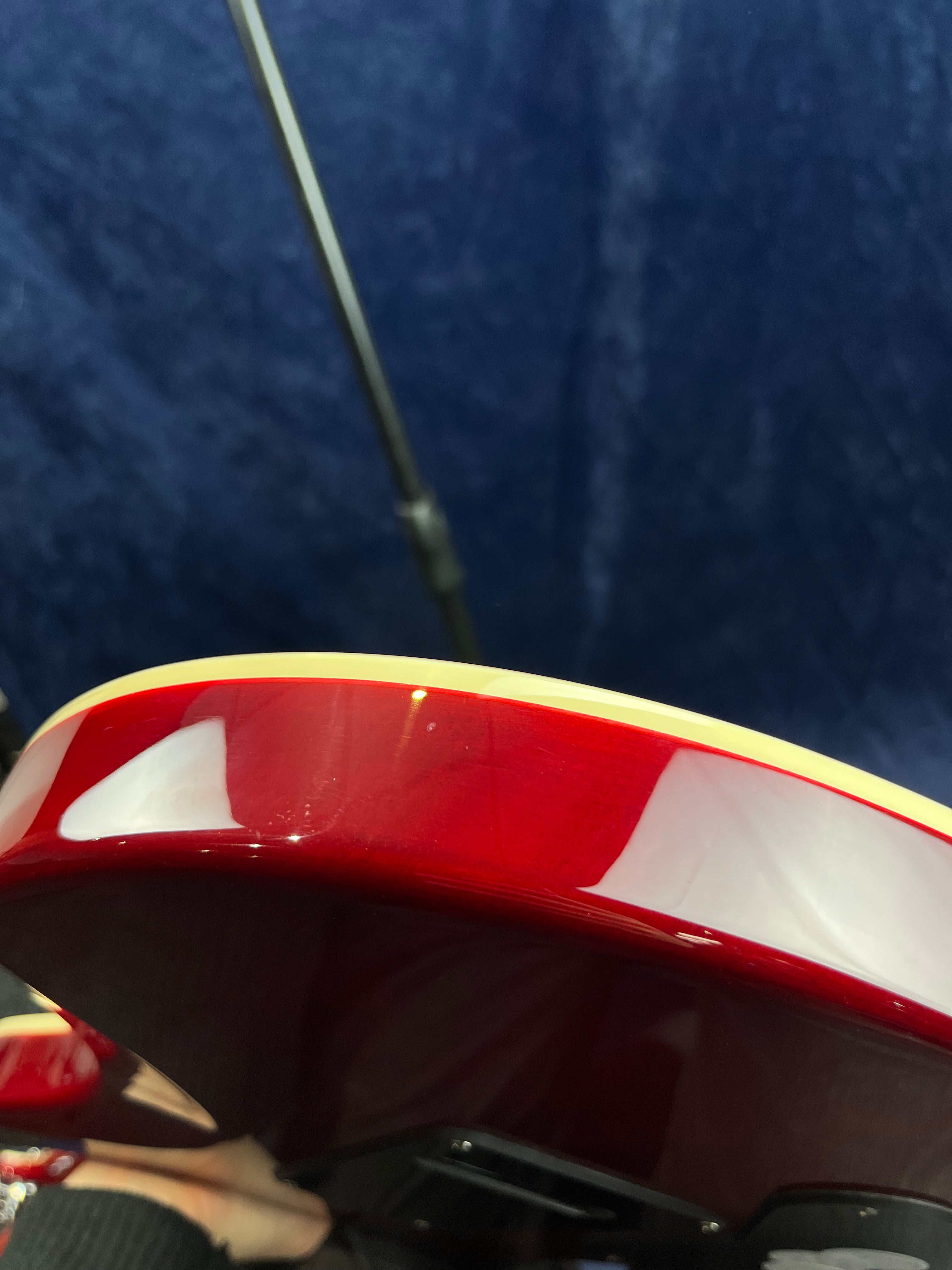 Close-up of a red electric guitar body edge with cream binding, showing a small dent or chip in the finish.