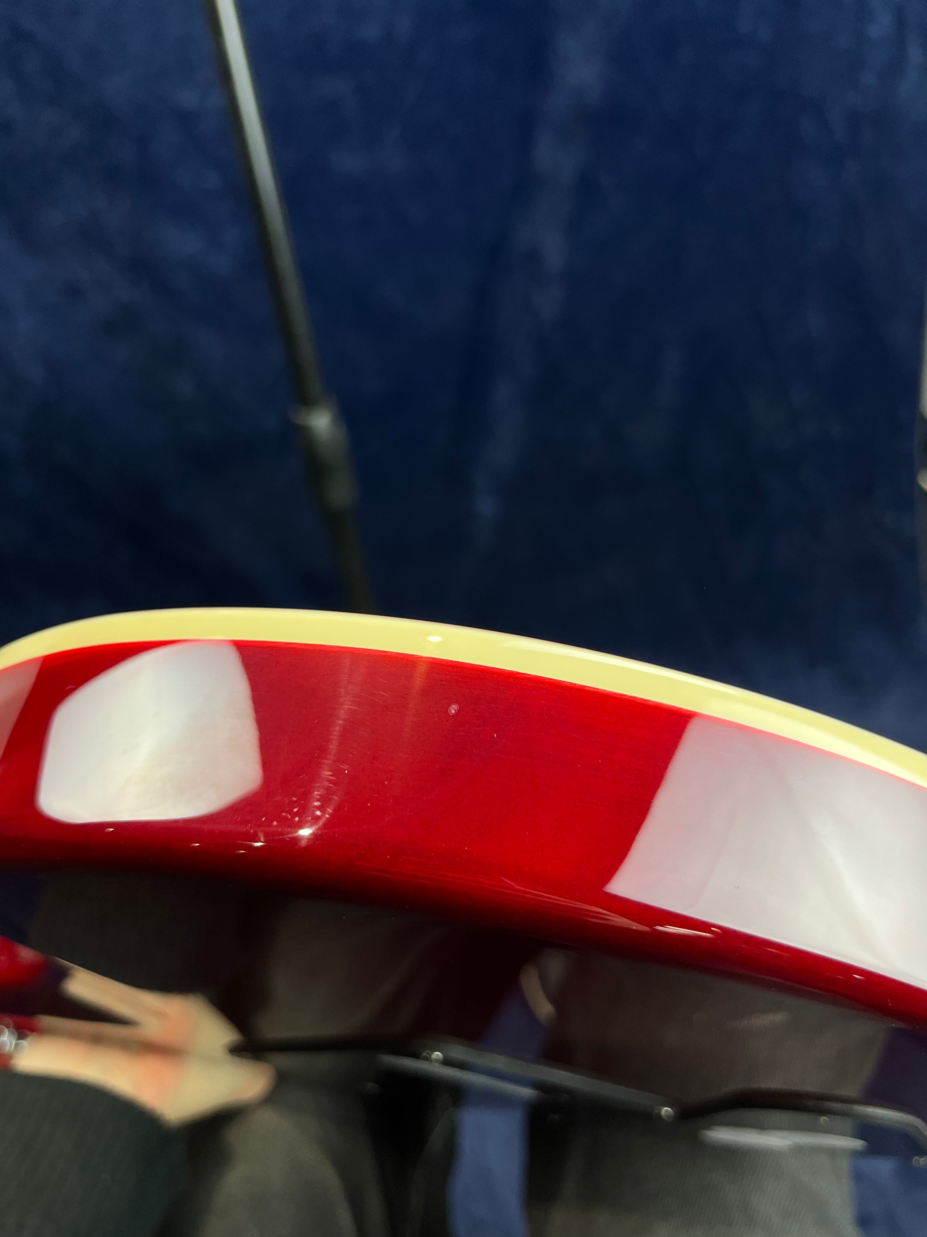 Red electric guitar body edge with cream binding, showing a shiny finish and reflection of light, against a dark blue background.