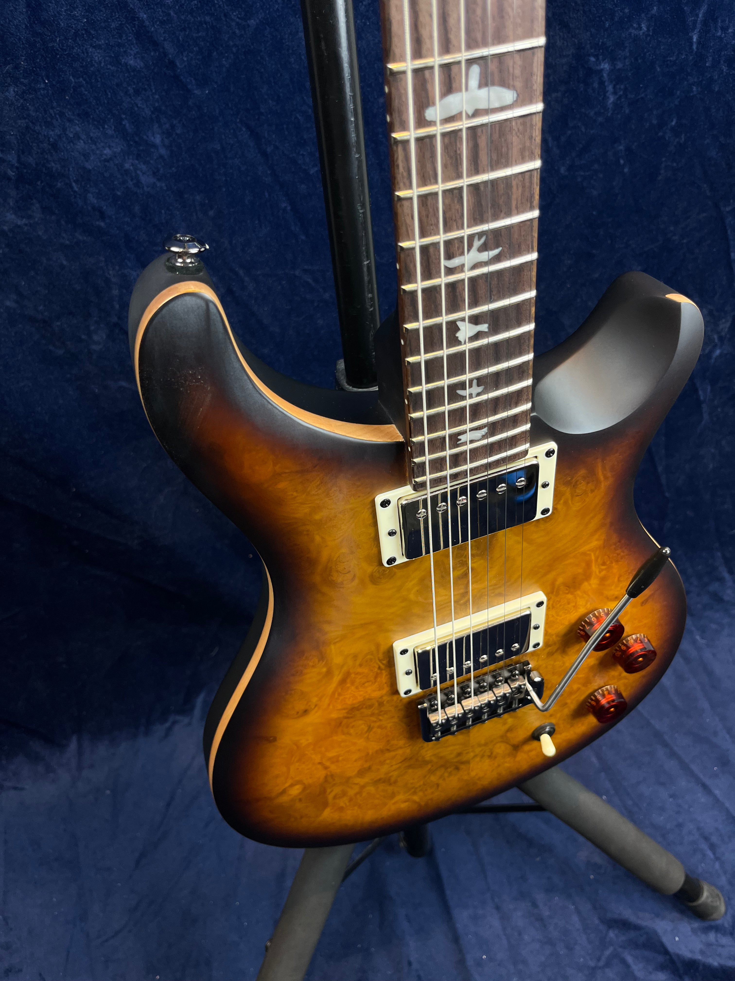 Electric guitar with a sunburst wood grain finish, two humbucker pickups, bird inlays on the fretboard, and whammy bar.