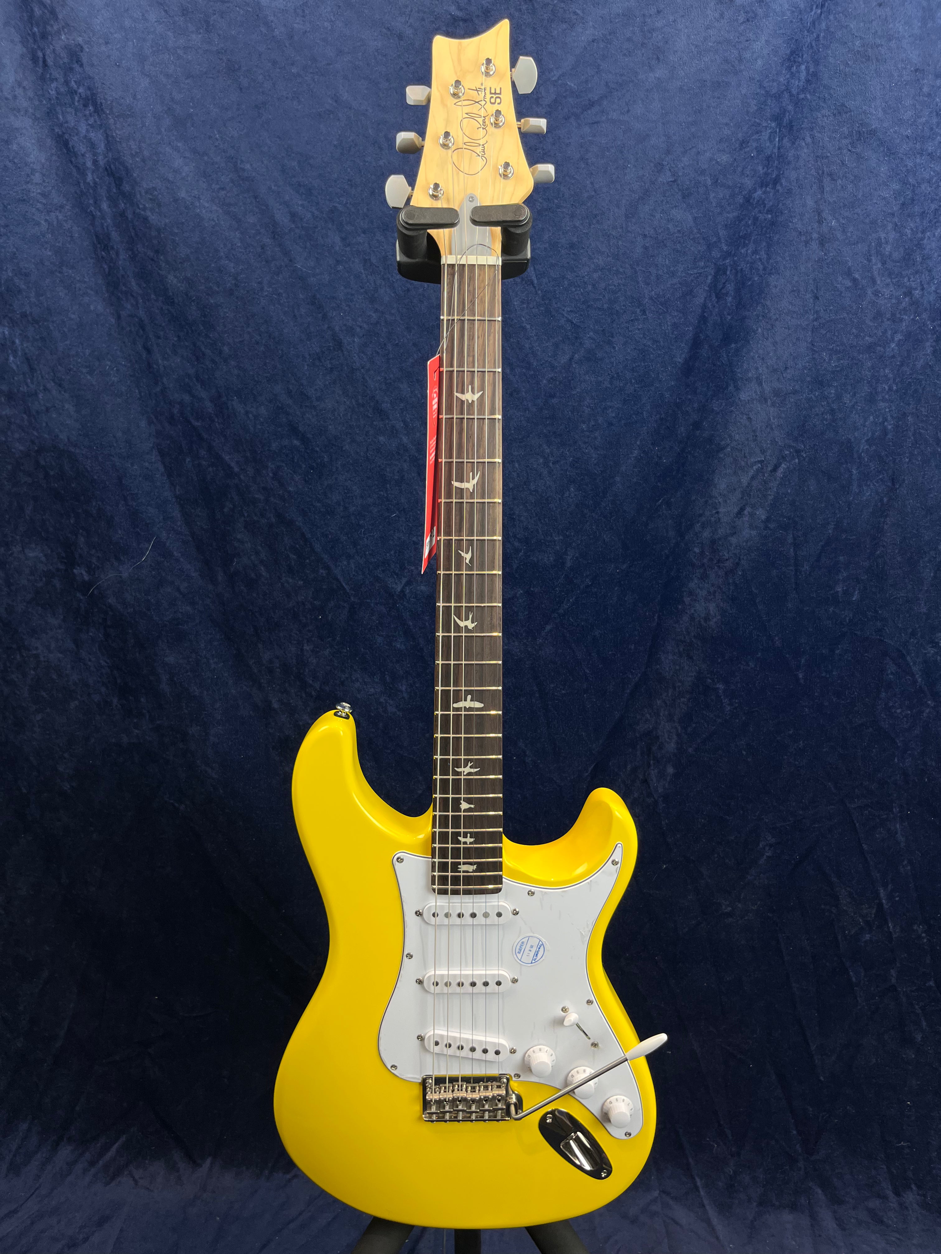 Bright yellow electric guitar with white pickguard, three pickups, a whammy bar, and a dark fingerboard featuring bird-shaped inlays.