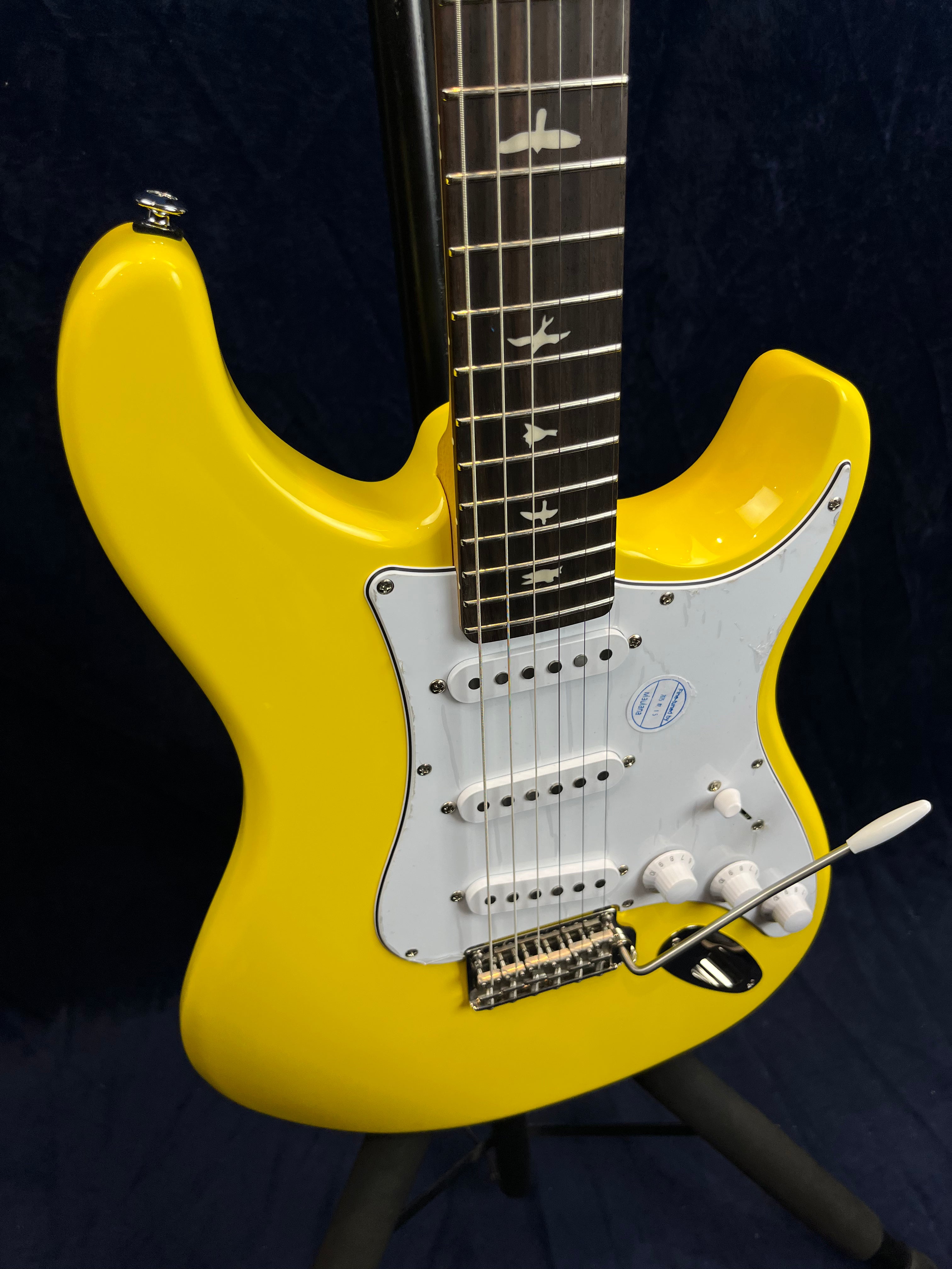 Bright yellow electric guitar with a white pickguard, three single-coil pickups, and bird inlays on the dark fretboard.