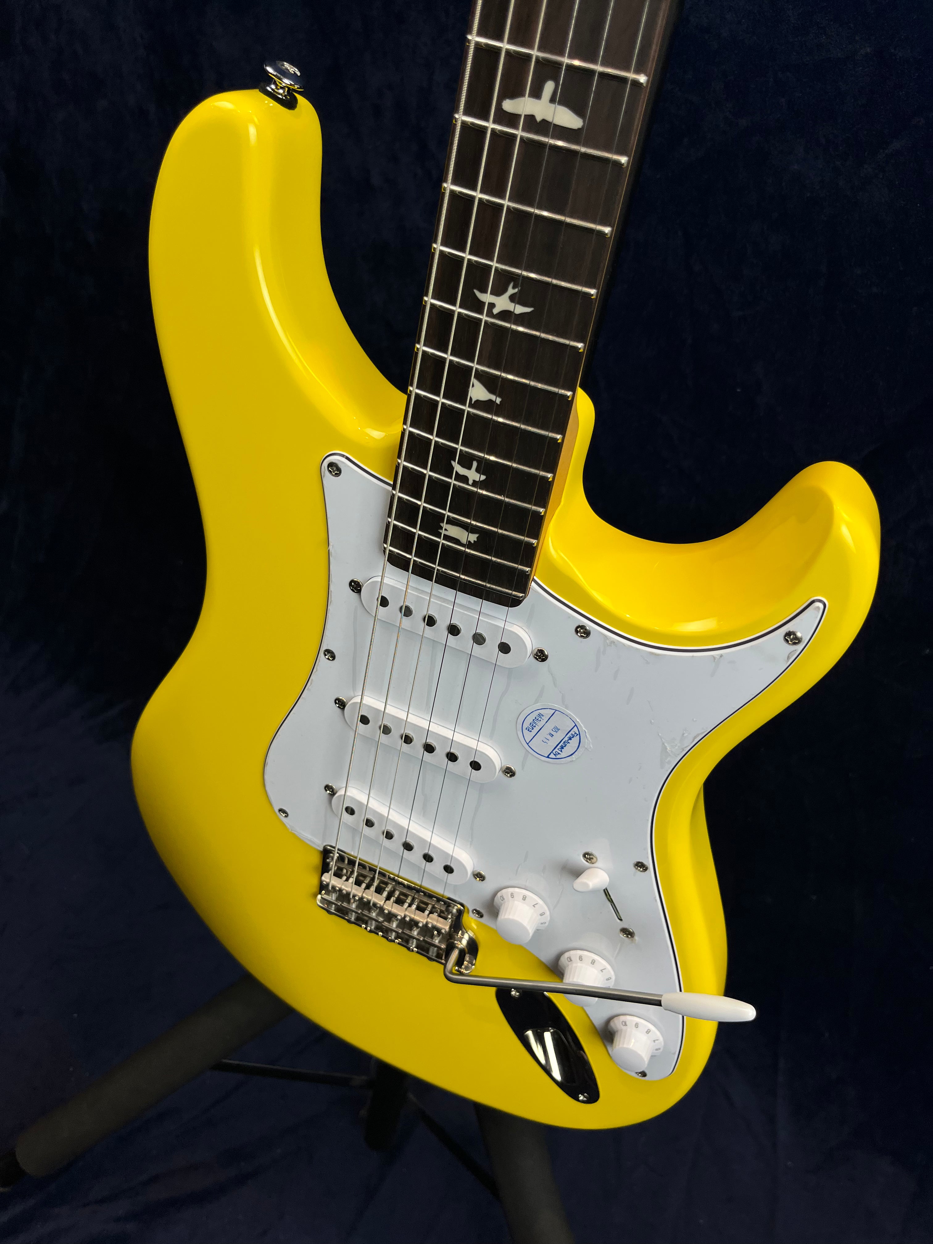 Bright yellow electric guitar with a white pickguard, three single-coil pickups, white controls, and bird-shaped inlays on a dark fingerboard.