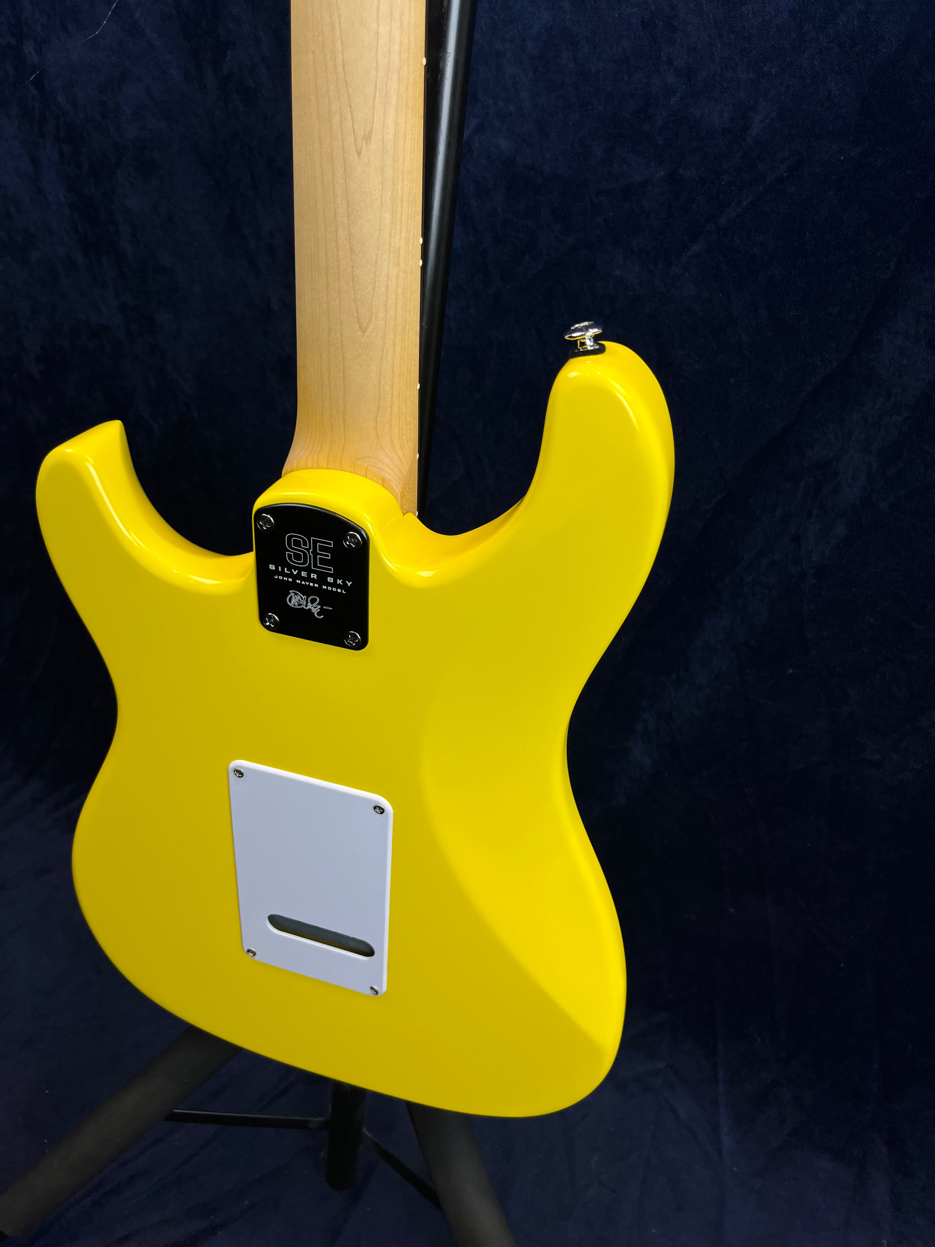 Bright yellow electric guitar viewed from the back, showing a natural wood neck and white plastic cover plate near the bottom.