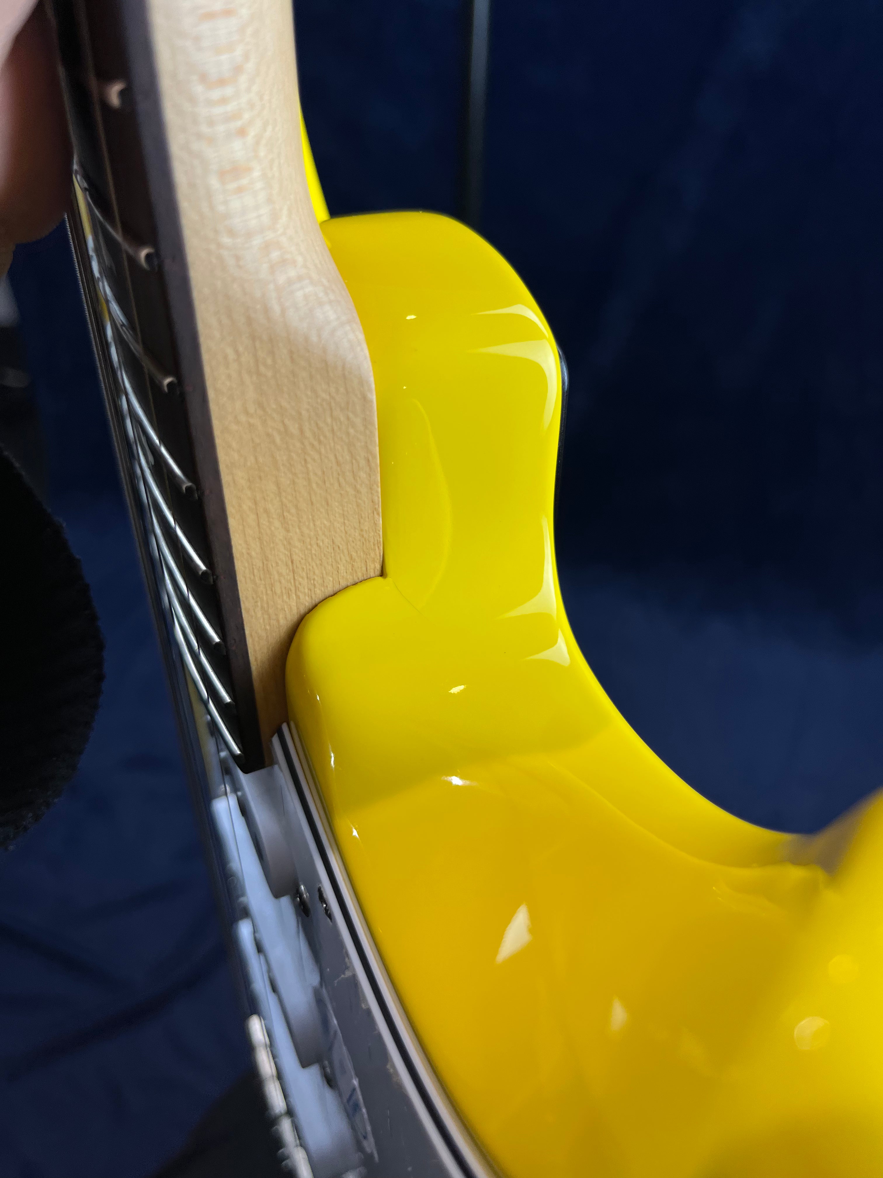 Close-up of an electric guitar showing the glossy yellow body and the natural wood neck joint with visible metal frets.