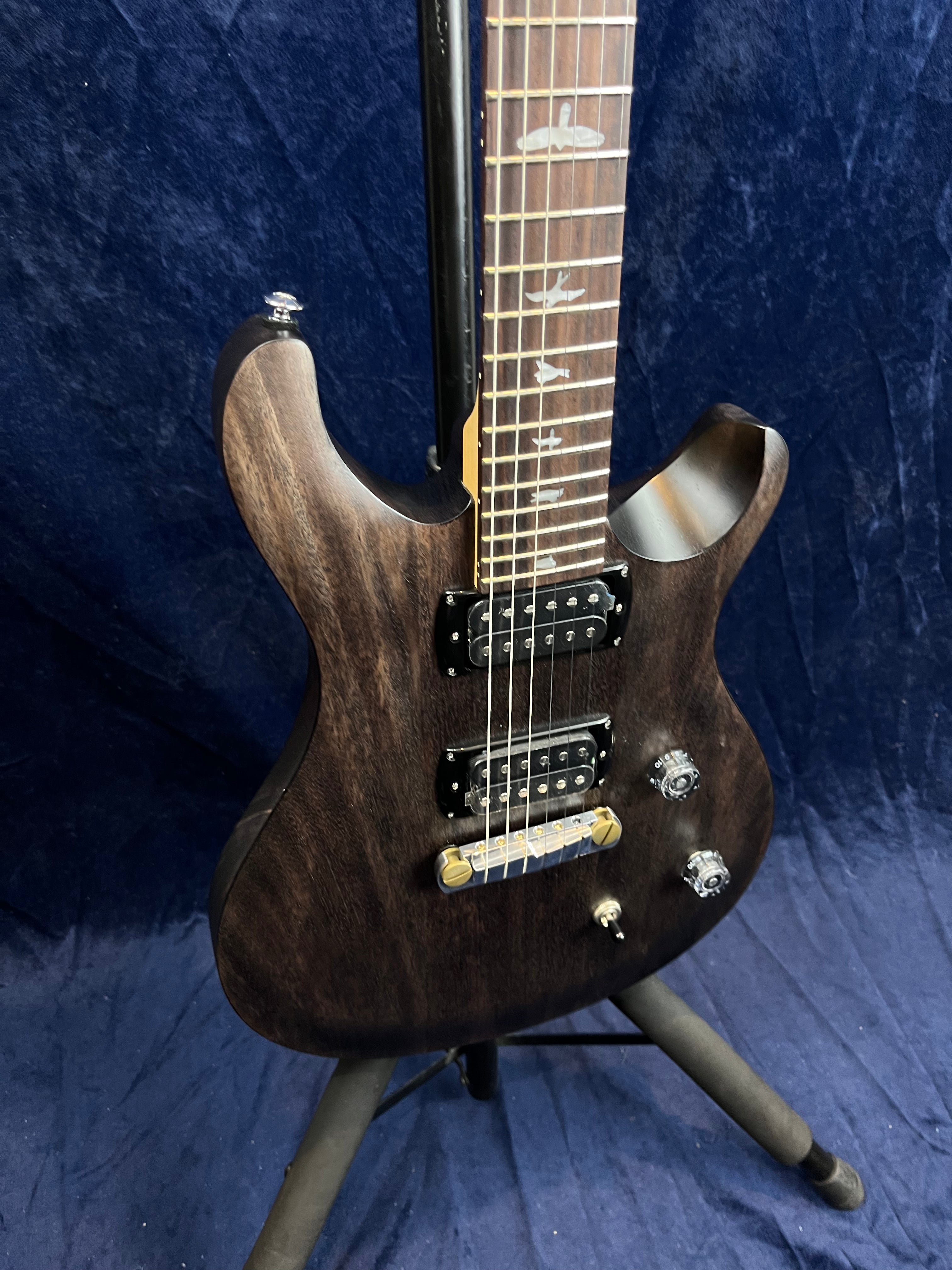 Dark wood electric guitar with two humbucker pickups, two control knobs, a pickup switch, and bird inlays on the fretboard, shown on a stand.