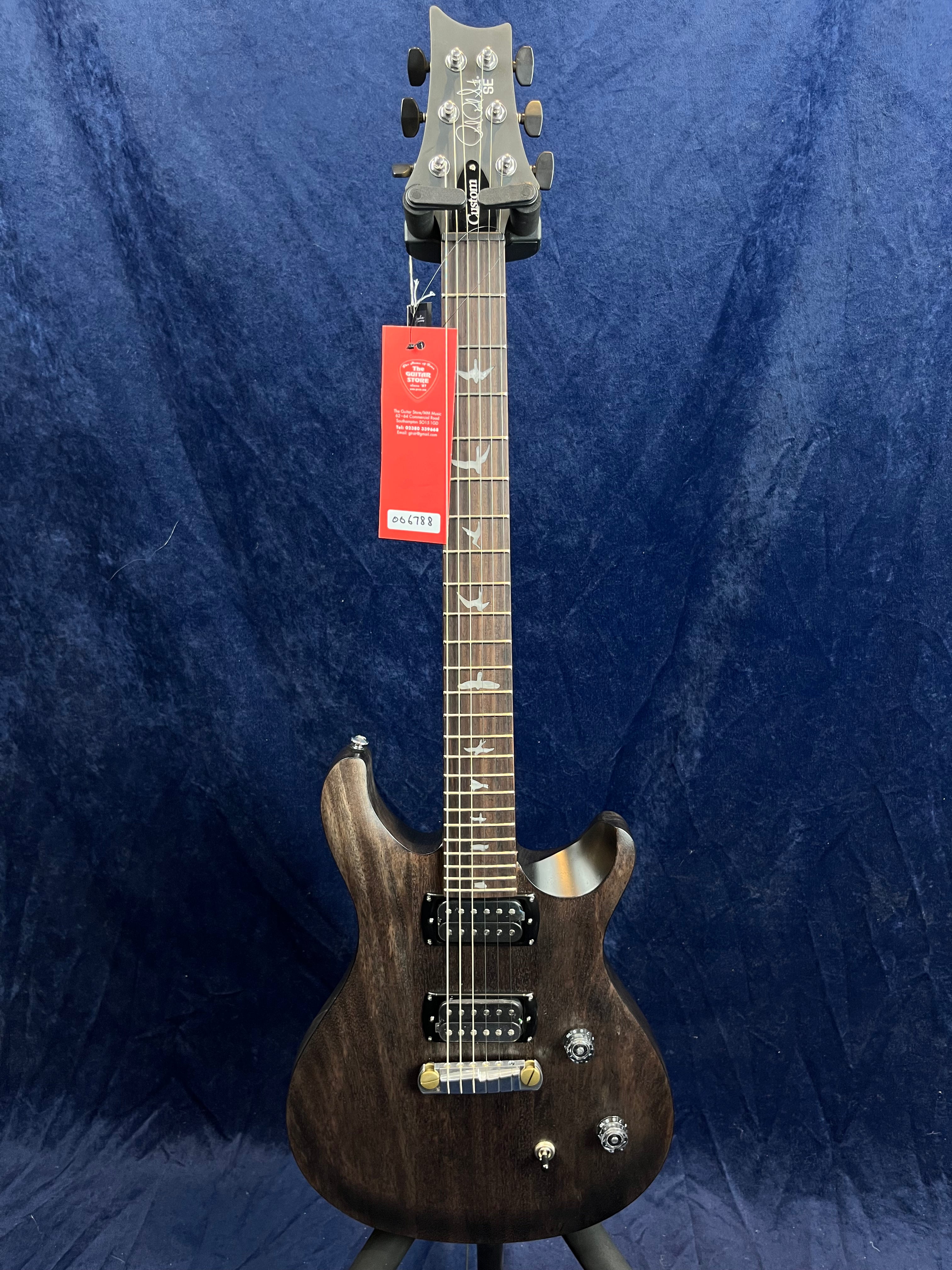 Dark wood electric guitar with two humbucker pickups, bird inlays on the fretboard, three control knobs, and a red tag hanging near the headstock.