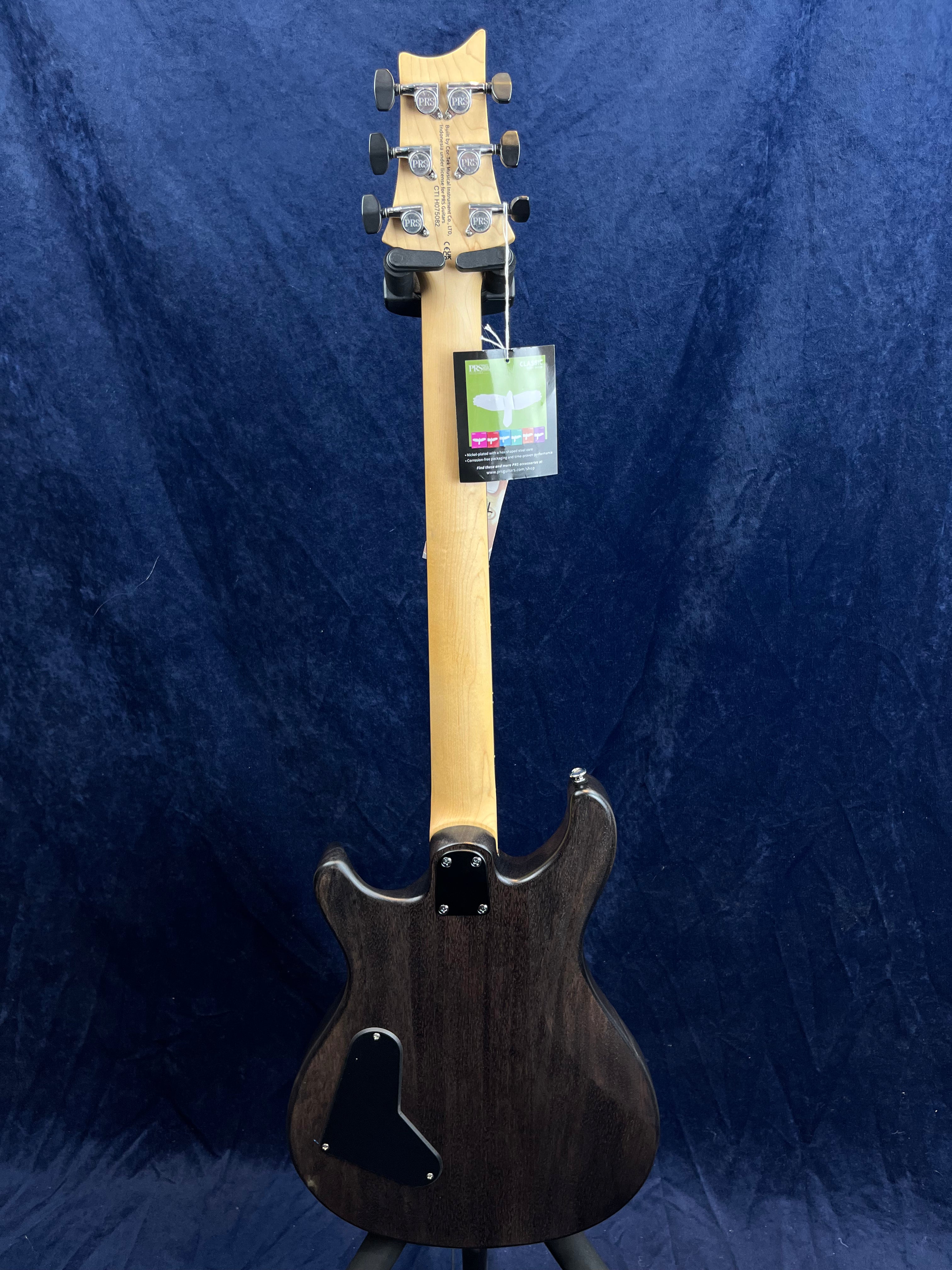 Electric guitar shown from the back, with a natural wood neck, dark wood body, six tuning pegs, and a hang tag attached near the headstock.
