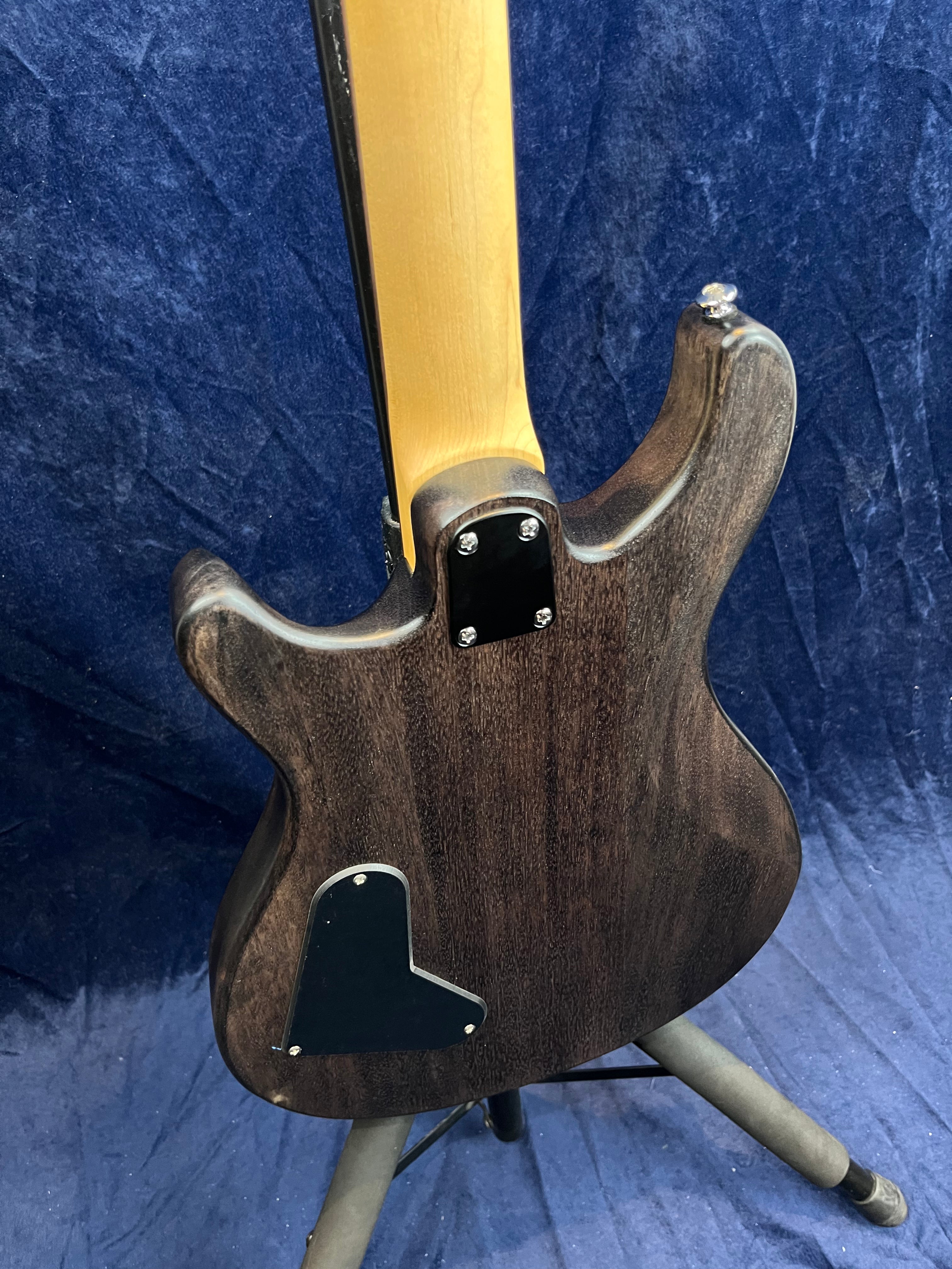 Back view of a dark wood electric guitar showing the neck joint, metal plate with screws, and a black electronics cover plate on the body.