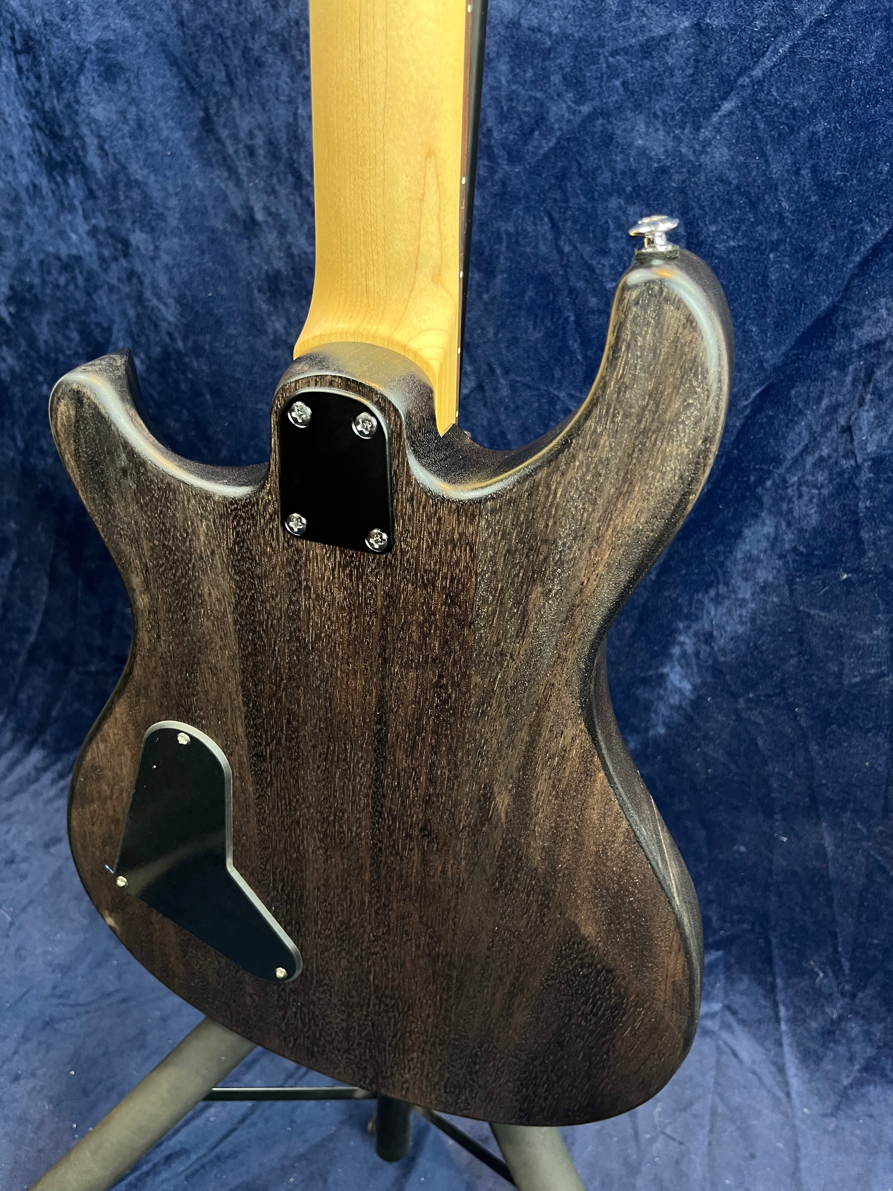 Rear view of an electric guitar showing a dark wood body, bolt-on maple neck, and black control cavity covers against a dark blue background.
