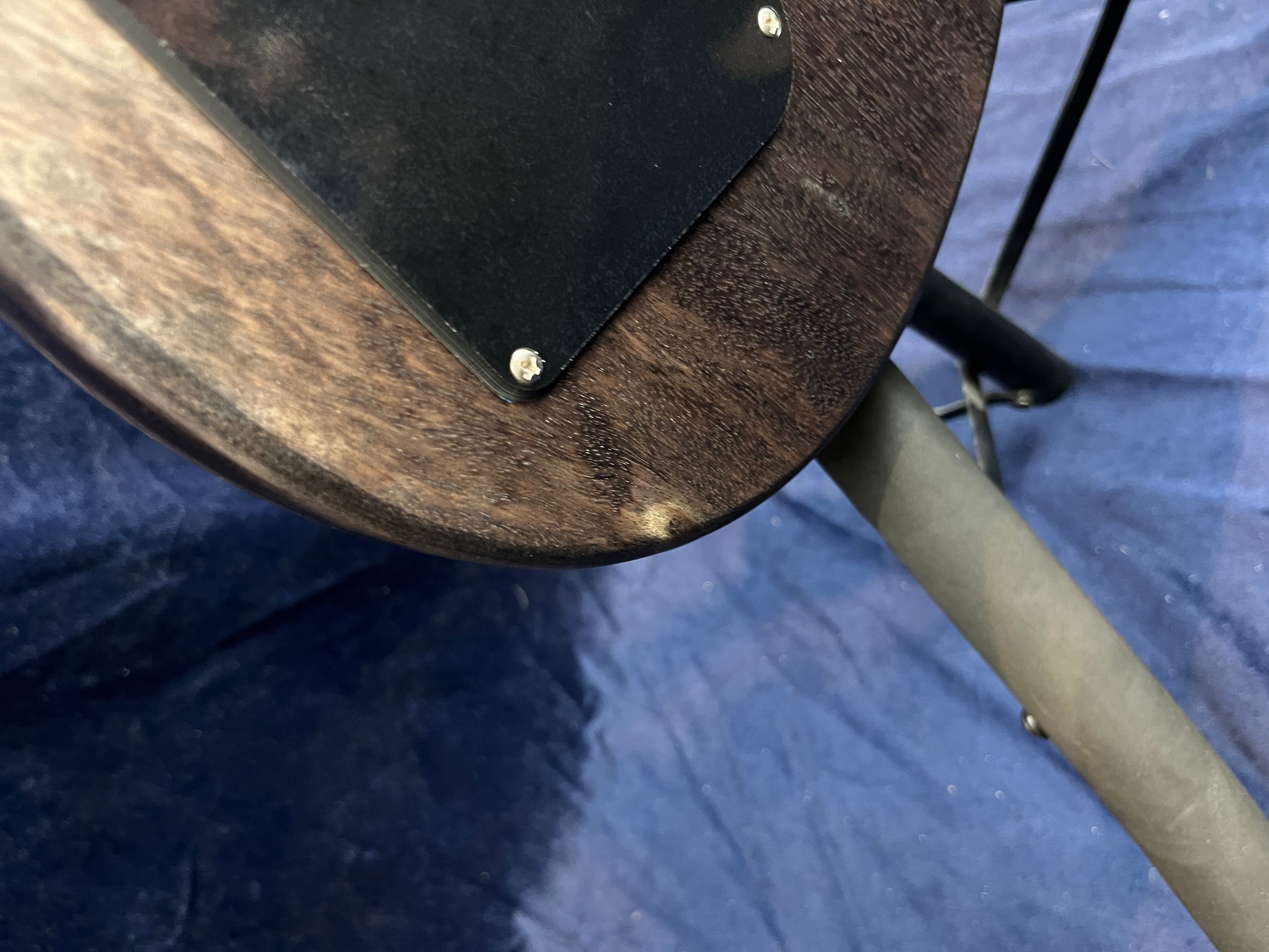 Close-up of a dark wood electric guitar body showing a small chip in the finish near the edge and a corner of the black plastic electronics cover.