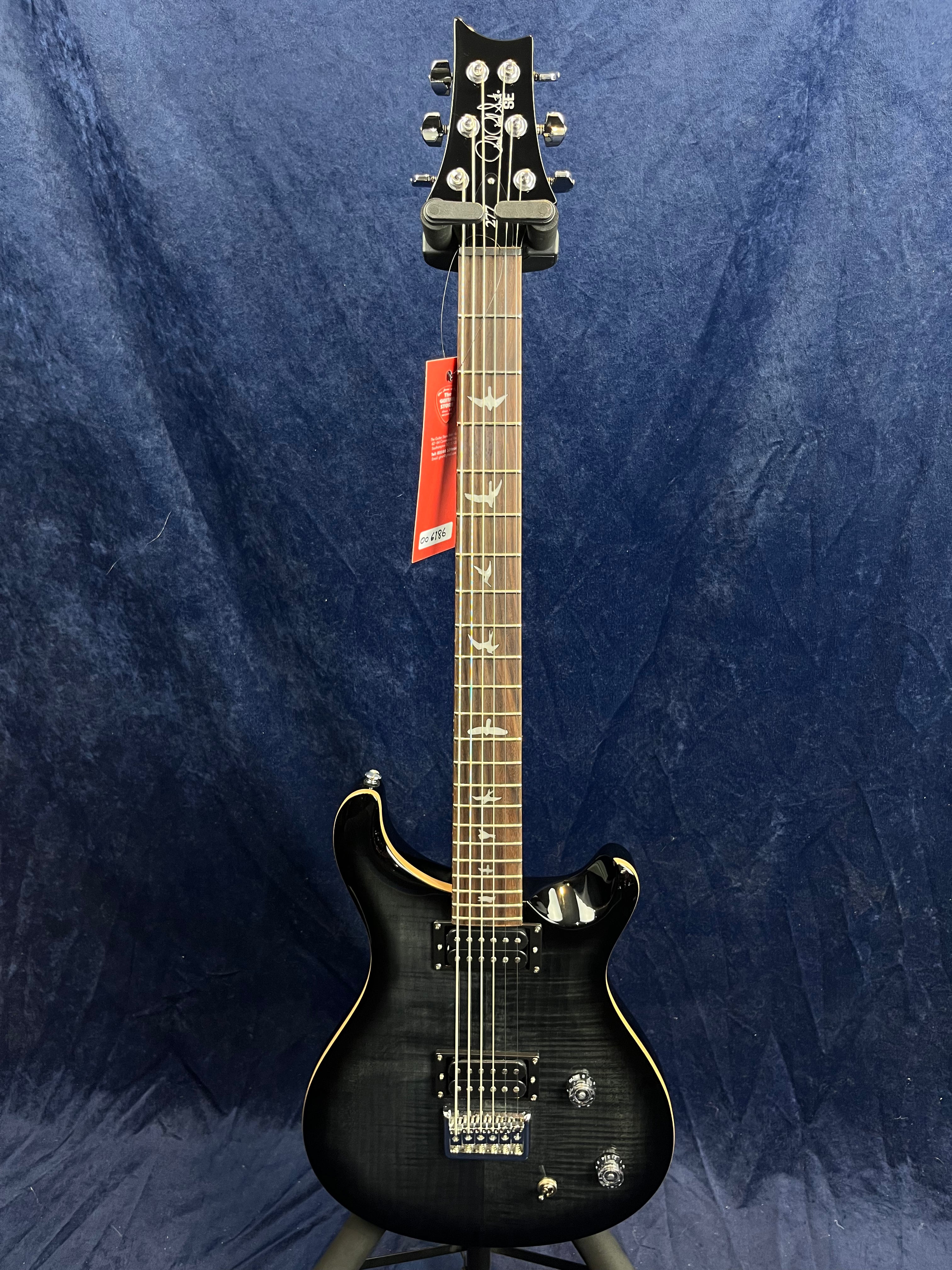 Glossy black electric guitar with bird-shaped inlays on the fretboard, dual humbucker pickups, two knobs, and a red tag hanging from the headstock.