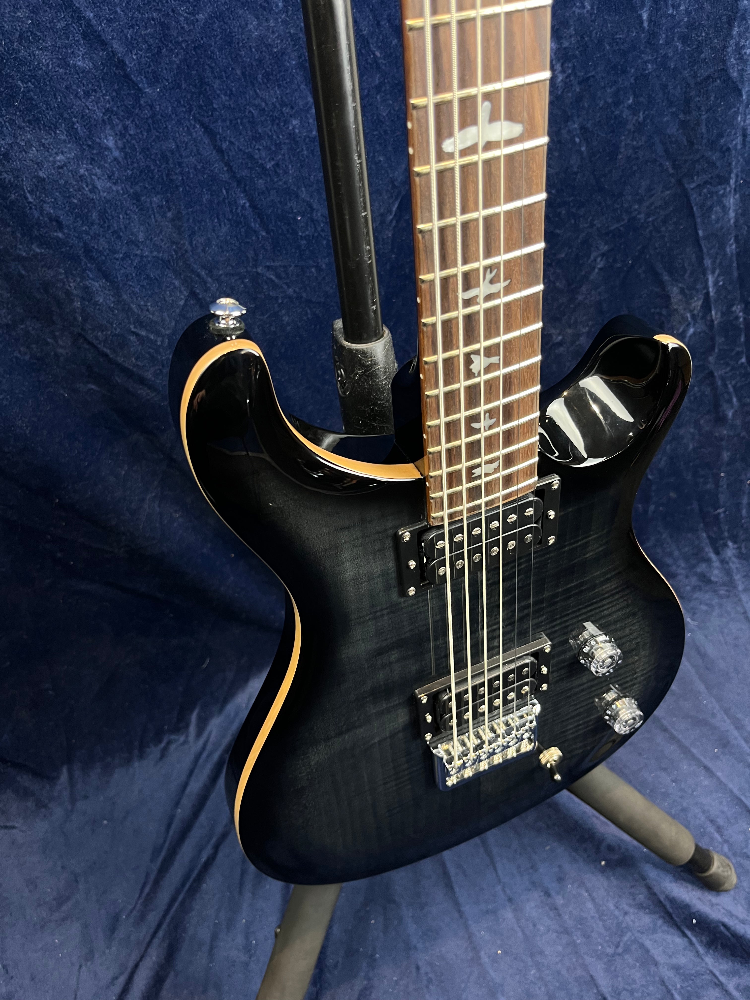 Black electric guitar with two humbucker pickups, clear control knobs, bird inlays on a rosewood fretboard, and natural wood binding on the body edges.