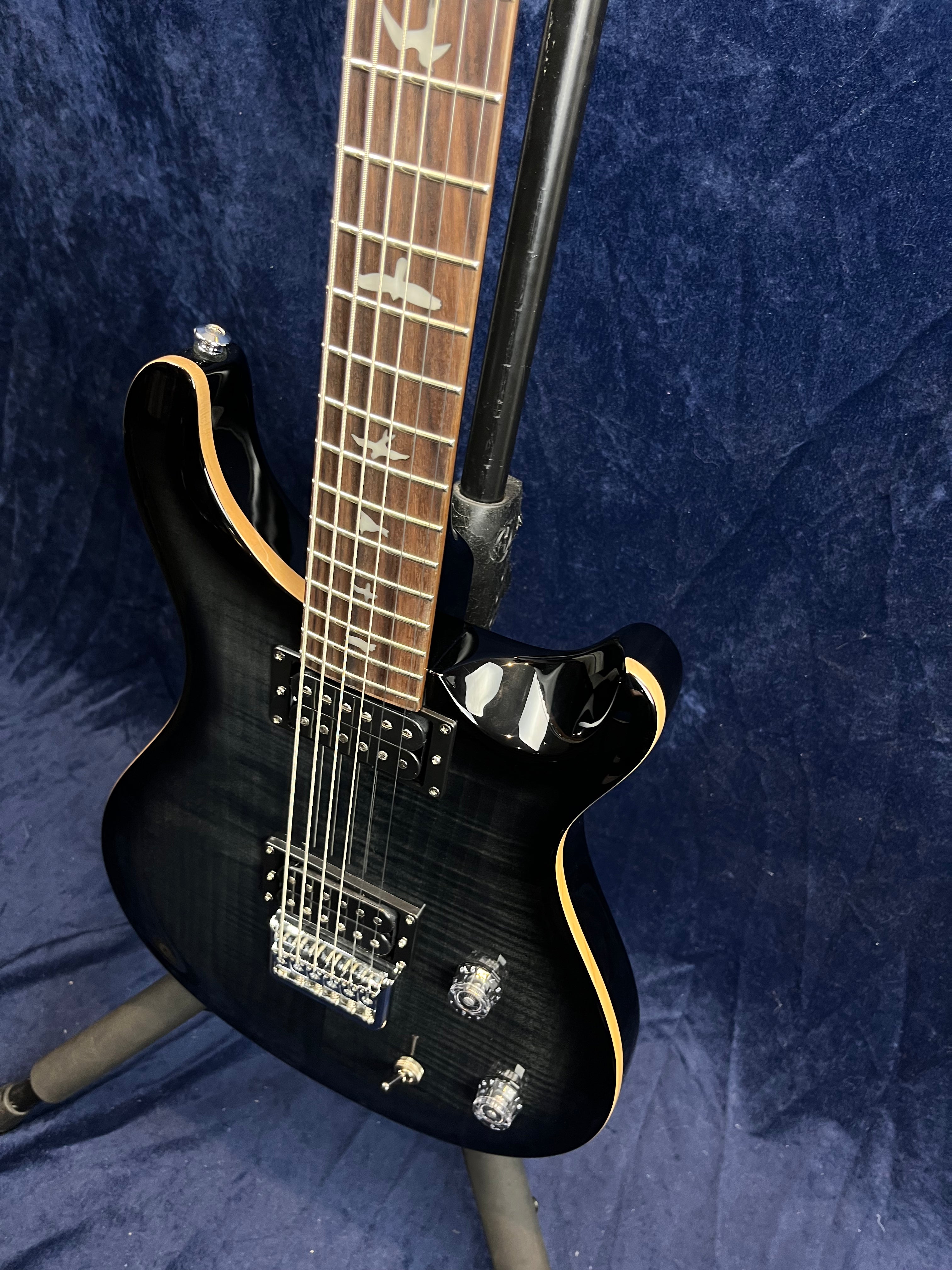 Black electric guitar with a glossy finish, two humbucker pickups, bird inlays on the fretboard, and chrome hardware, resting on a stand.