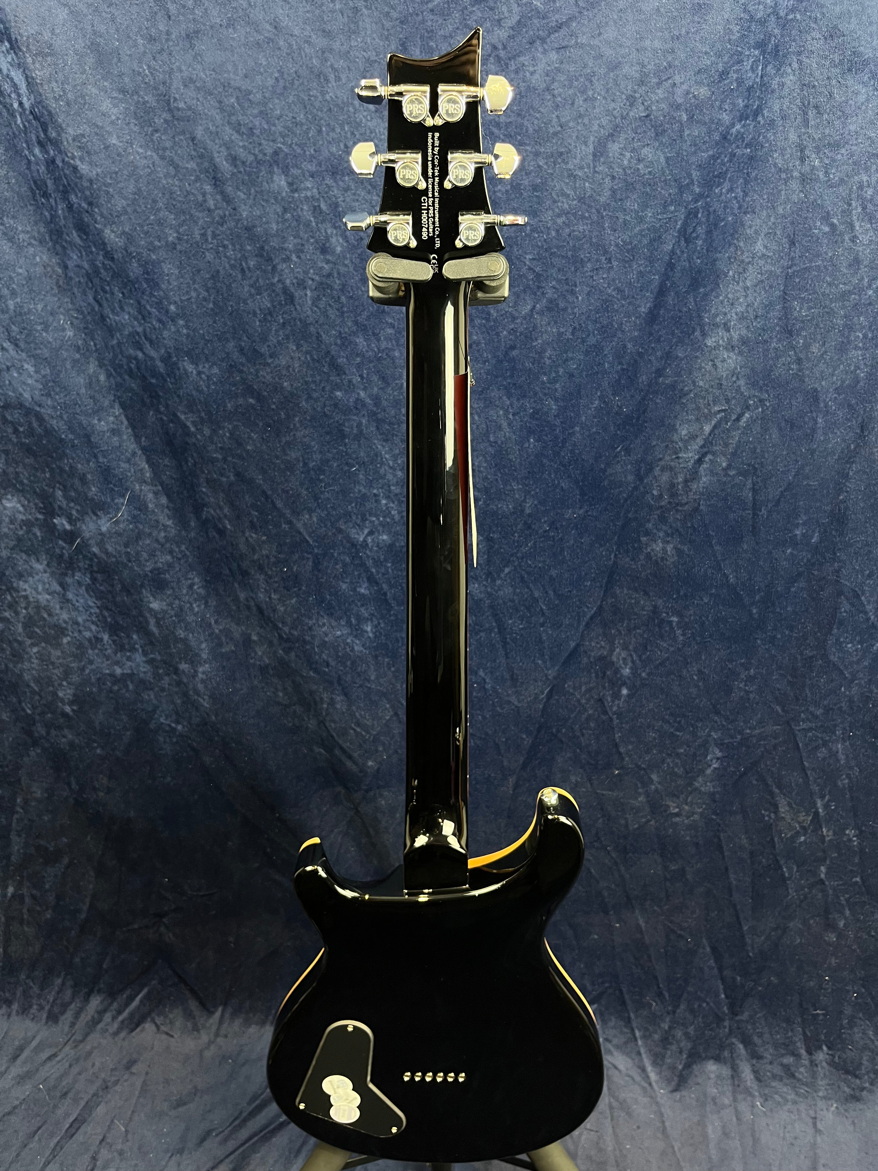 Black electric guitar shown from the back; shiny finish with six tuning pegs and a control cavity cover on the lower part of the body.