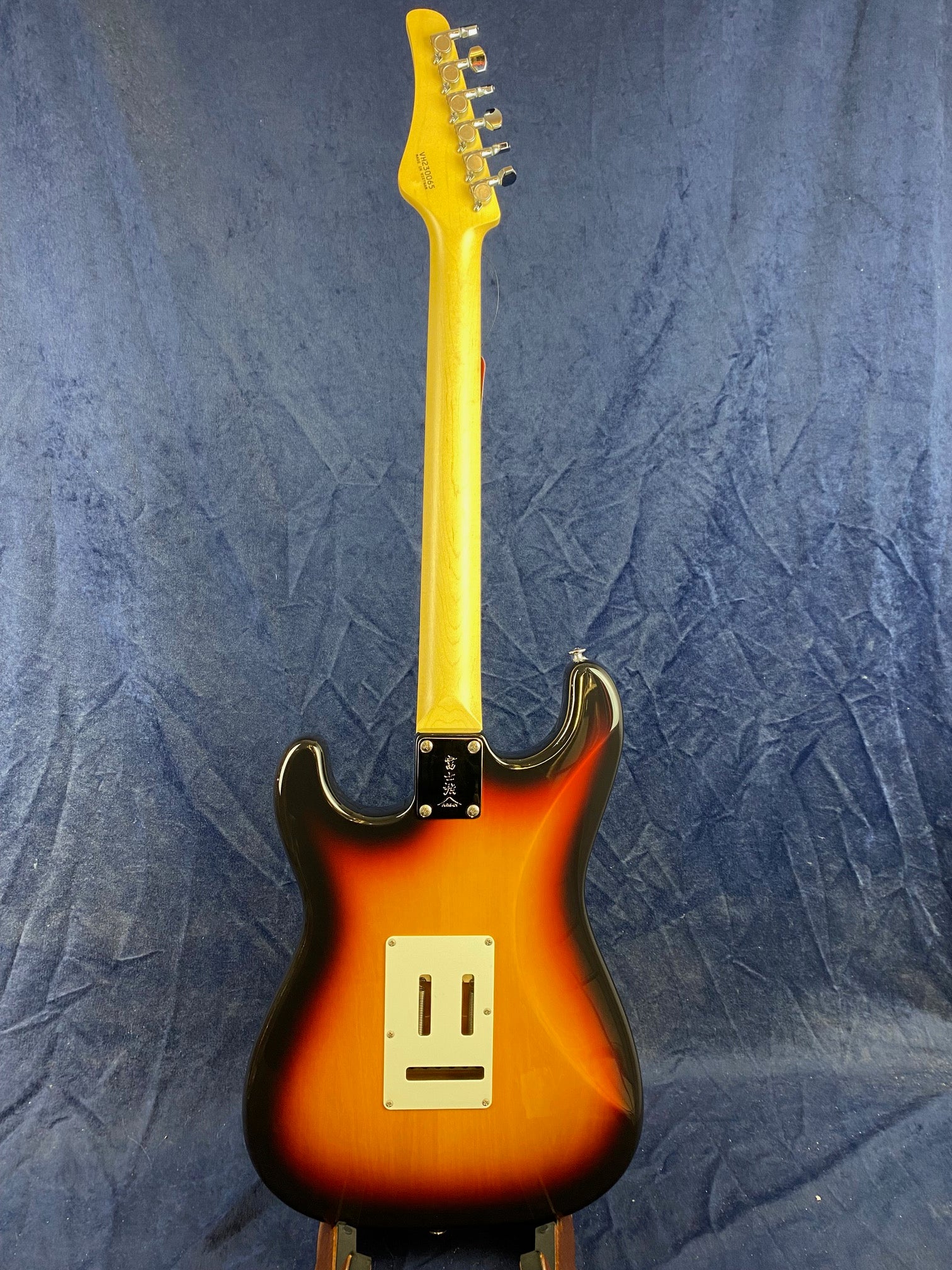 Sunburst electric guitar shown from the back, with a light wood neck, chrome tuners, and a white rectangular plate on the body.