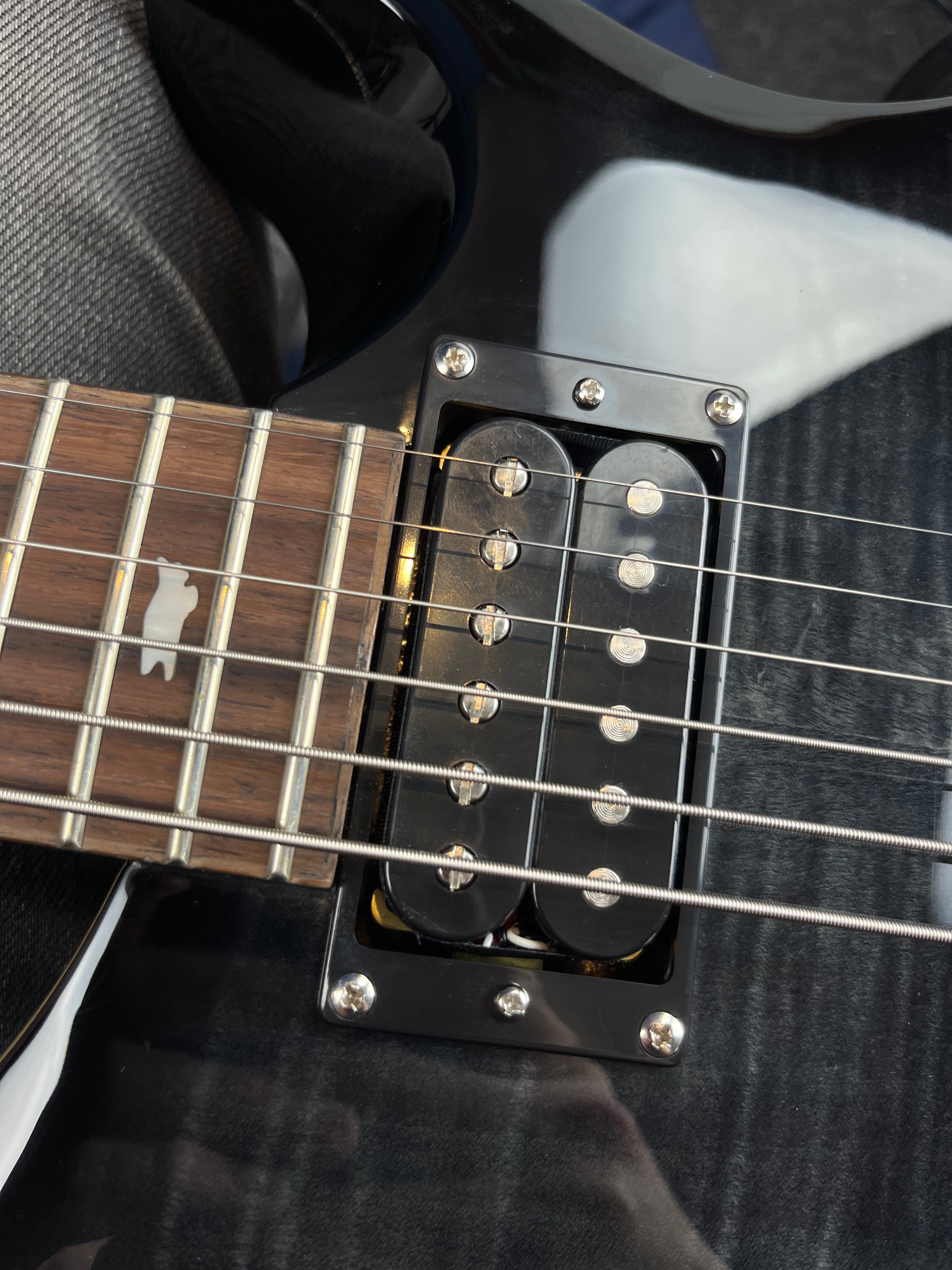 Close-up of an electric guitar showing 6 metal strings, a dual-coil humbucker pickup, and a rosewood fretboard with a bird-shaped inlay.