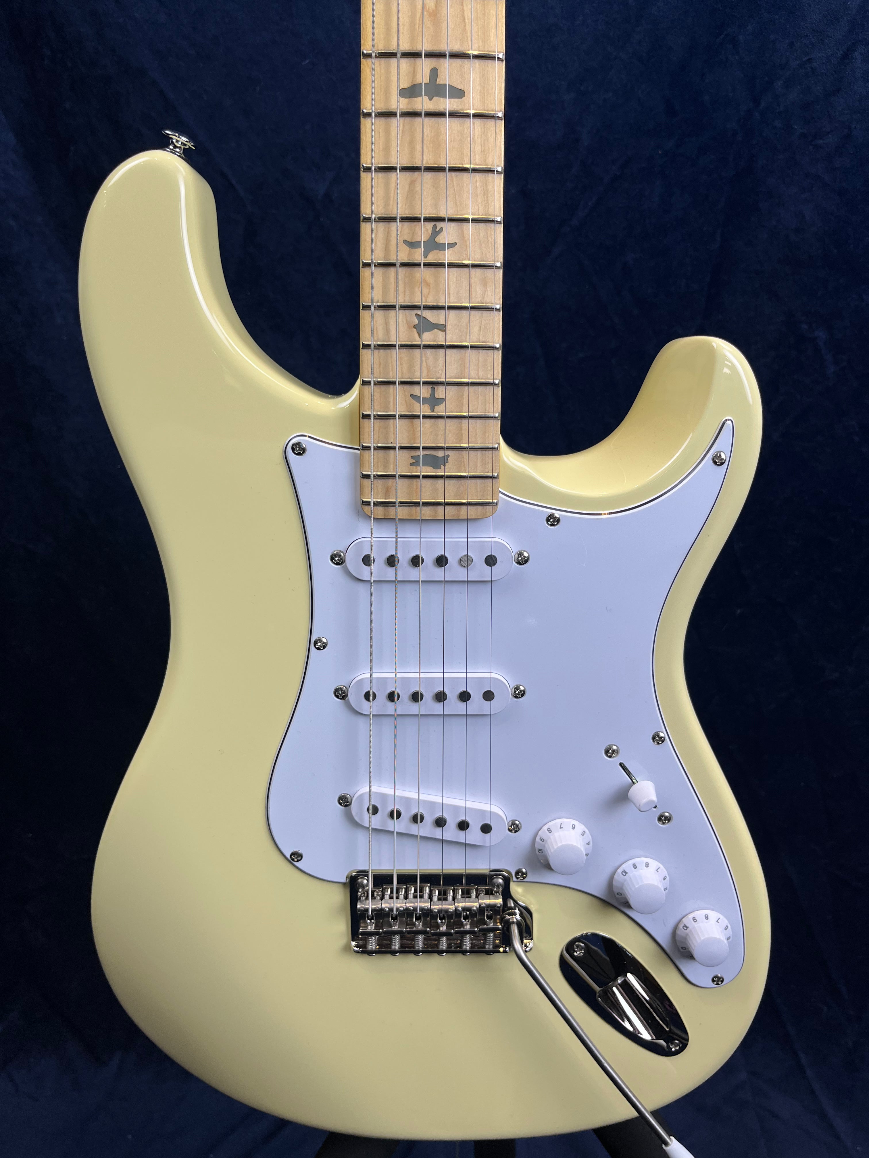 Cream-colored electric guitar with white pickguard, three single-coil pickups, three knobs, and maple neck featuring bird inlays on the fretboard.