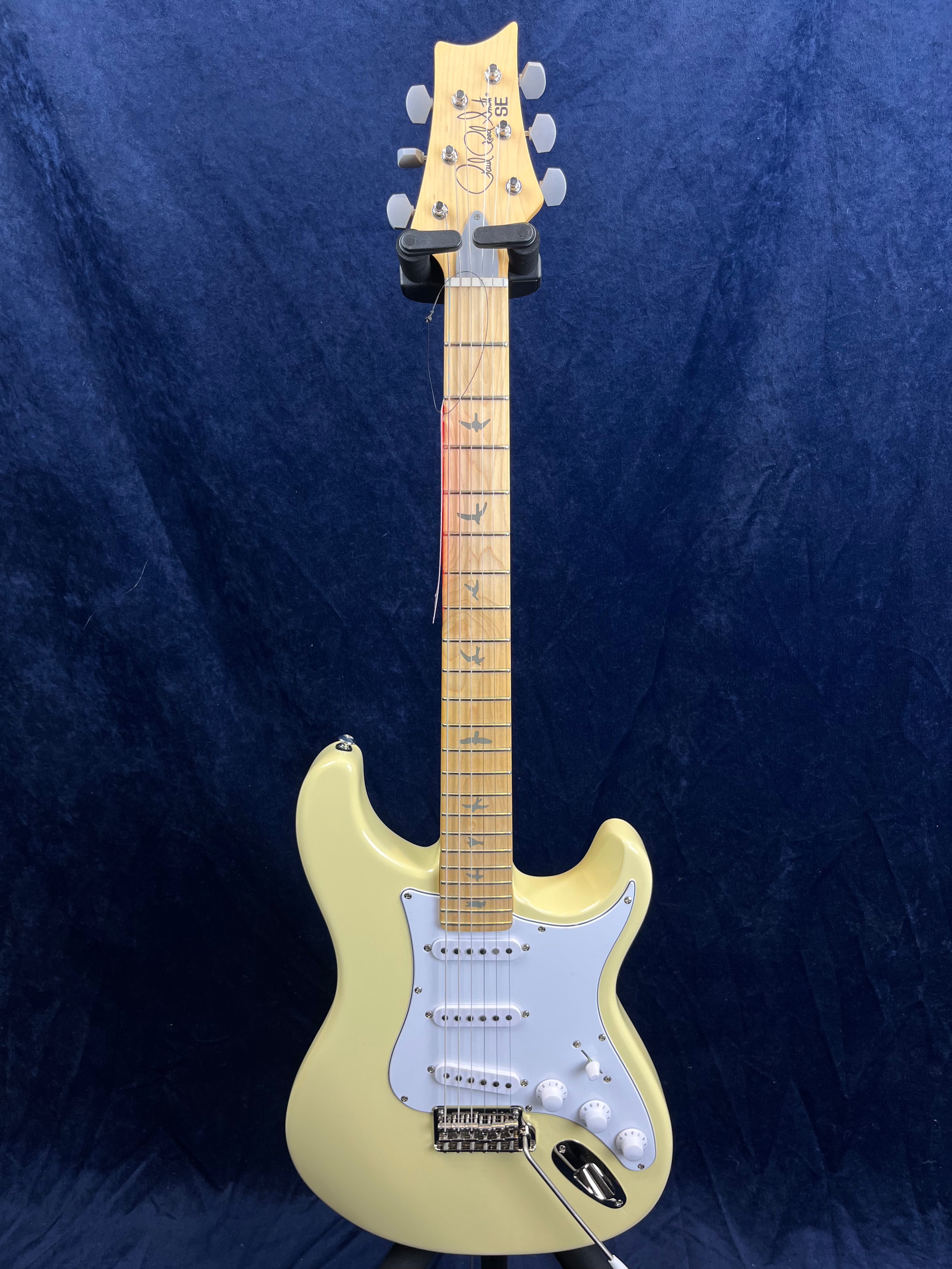 Cream-colored electric guitar with a white pickguard, maple neck, and bird-shaped inlays on the fretboard, displayed upright against a dark background.