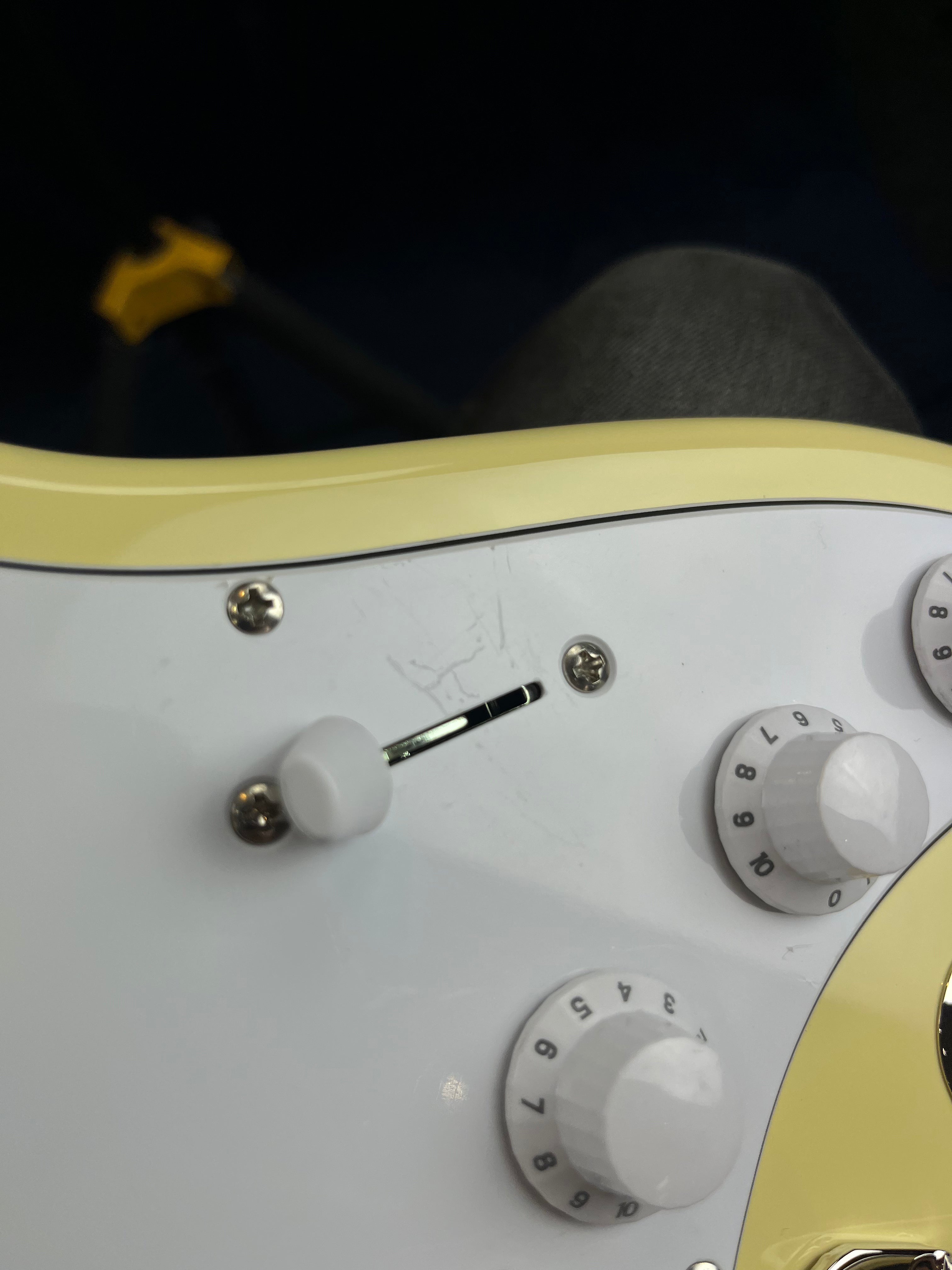 Close-up of an electric guitar showing white control knobs, a selector switch, and a white pickguard with light surface scratches.