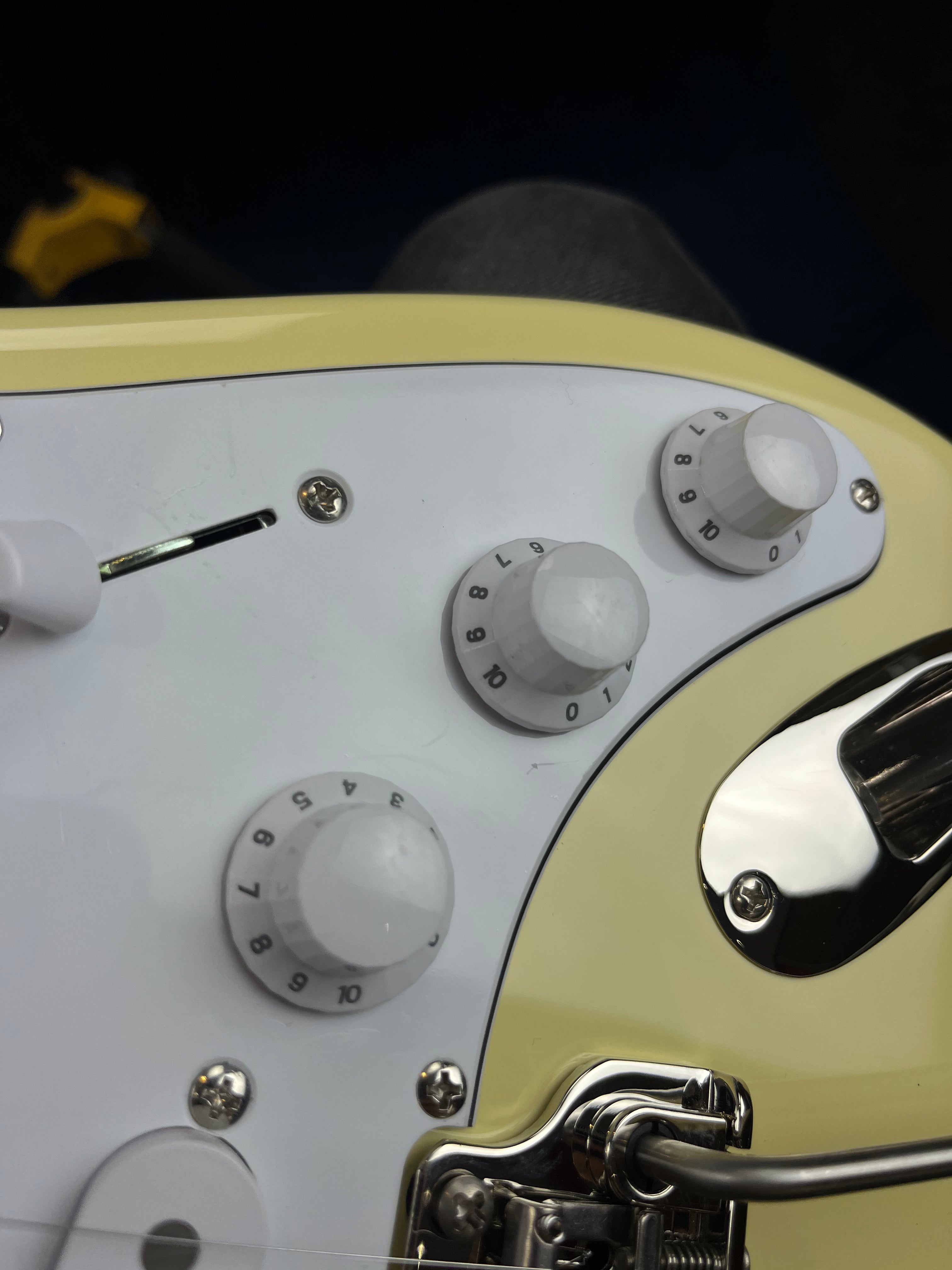 Three white control knobs labeled 1 to 10, a metal input jack, and a whammy bar on a cream electric guitar body with a white pickguard.