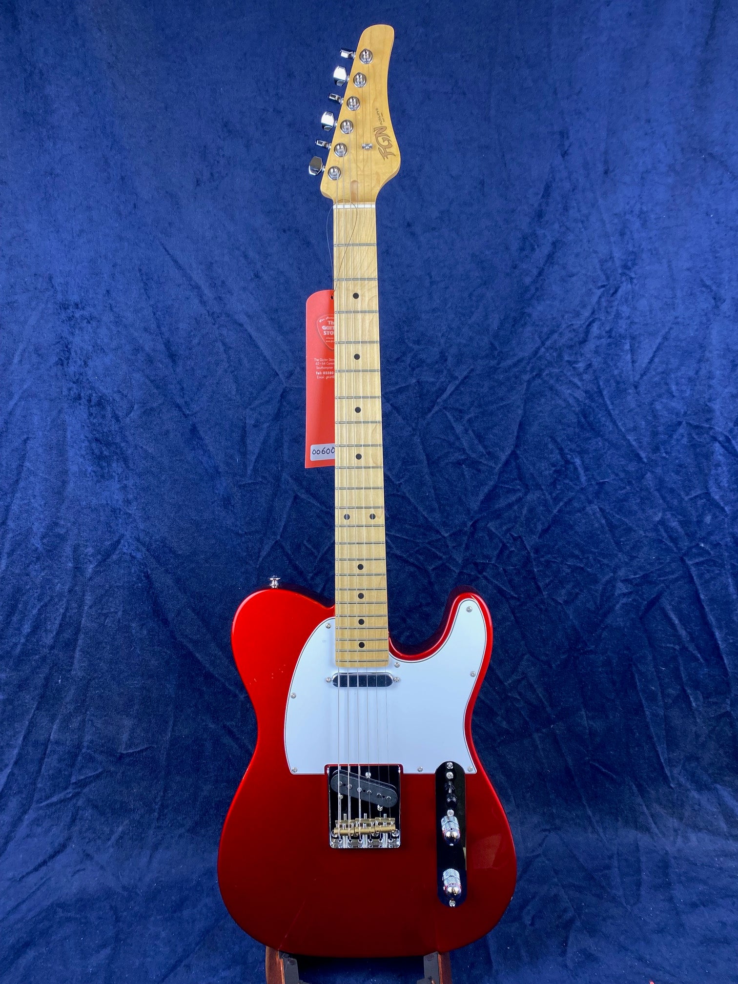 Red electric guitar with a white pickguard, chrome hardware, two pickups, and a light maple neck and fretboard against a solid blue background.