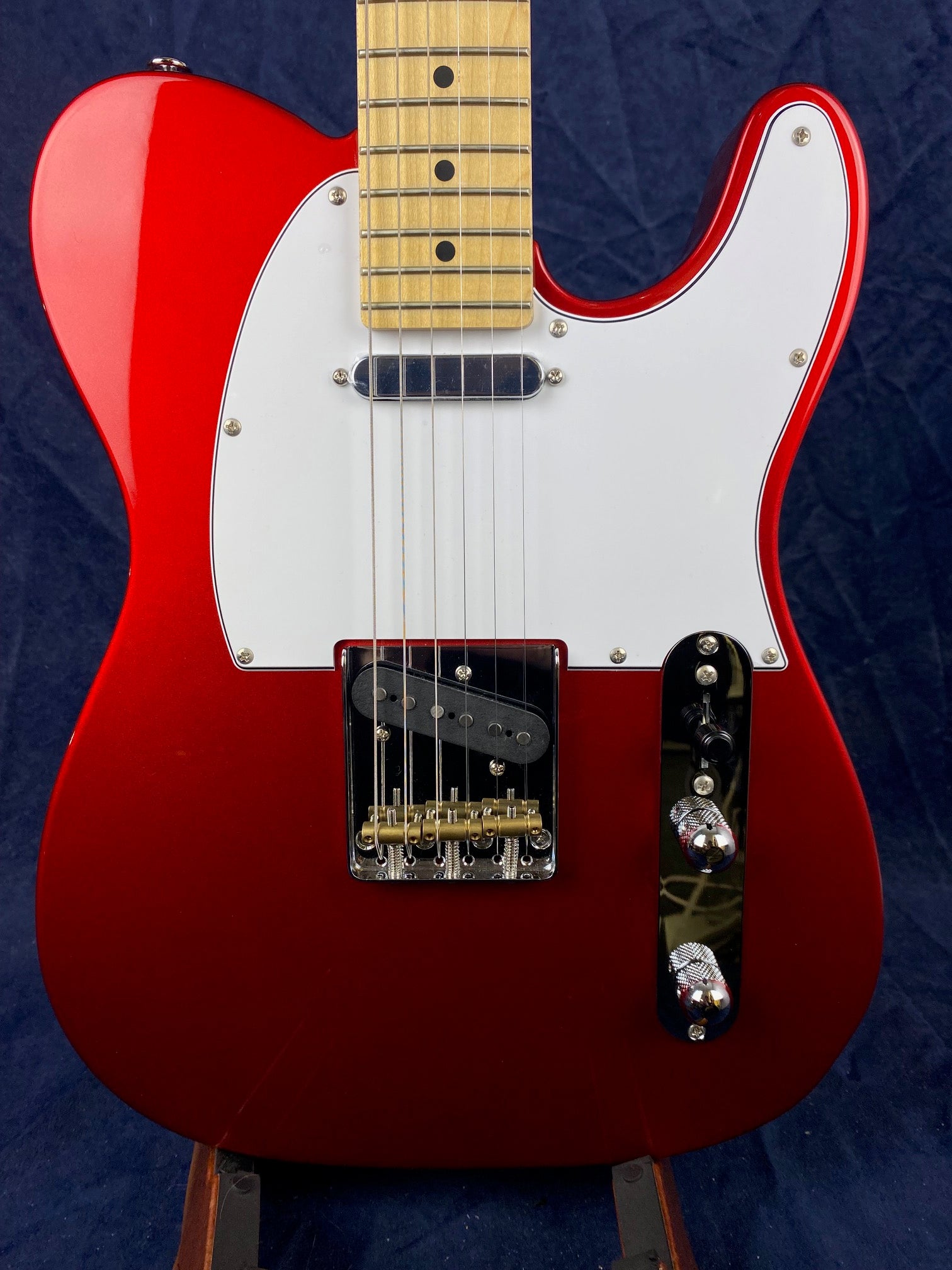 Red electric guitar with a white pickguard, chrome controls, two pickups, and a maple fretboard with black dot inlays.