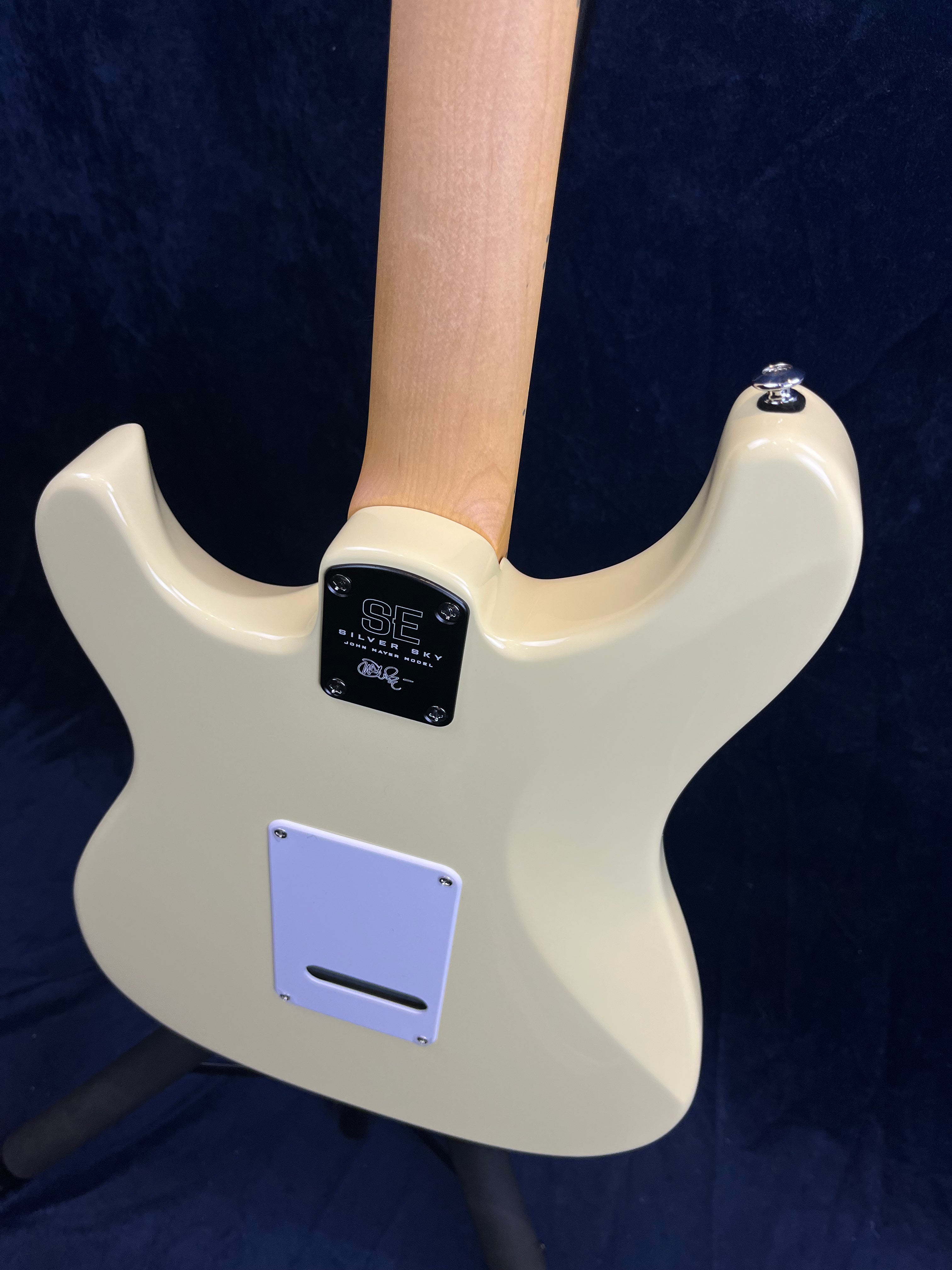 Cream-colored electric guitar shown from the back with a natural wood neck and a white access plate on a contoured body.