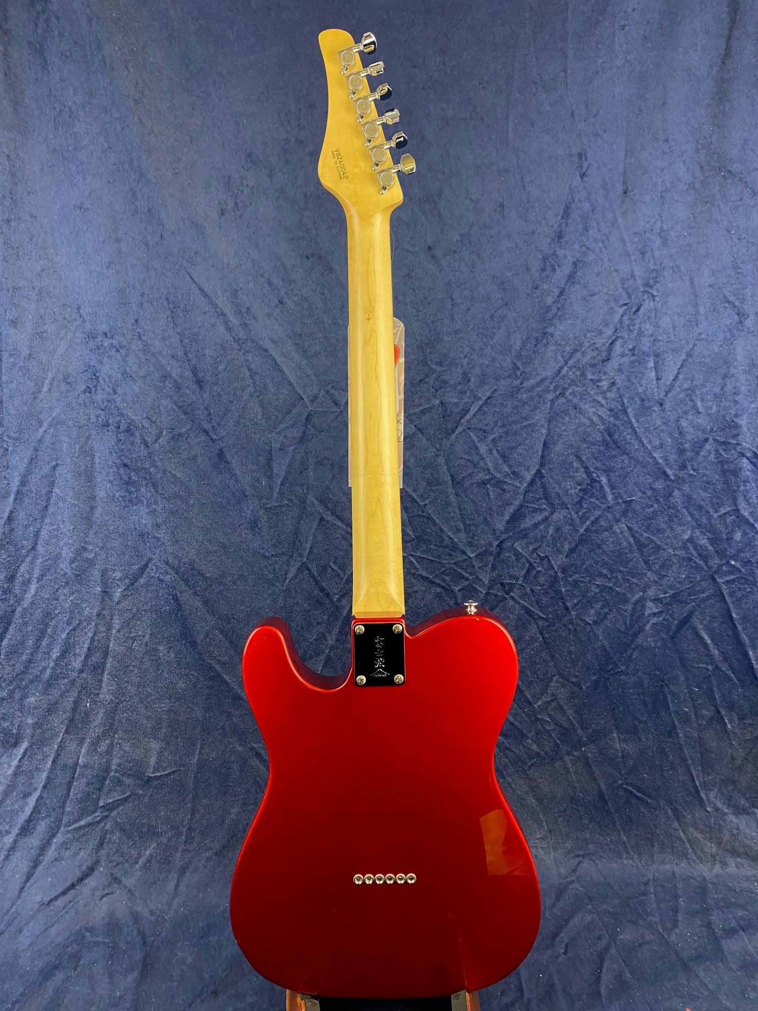 A red electric guitar viewed from the back, showing a light wood neck, six tuning pegs, and a glossy red body with string ferrules.