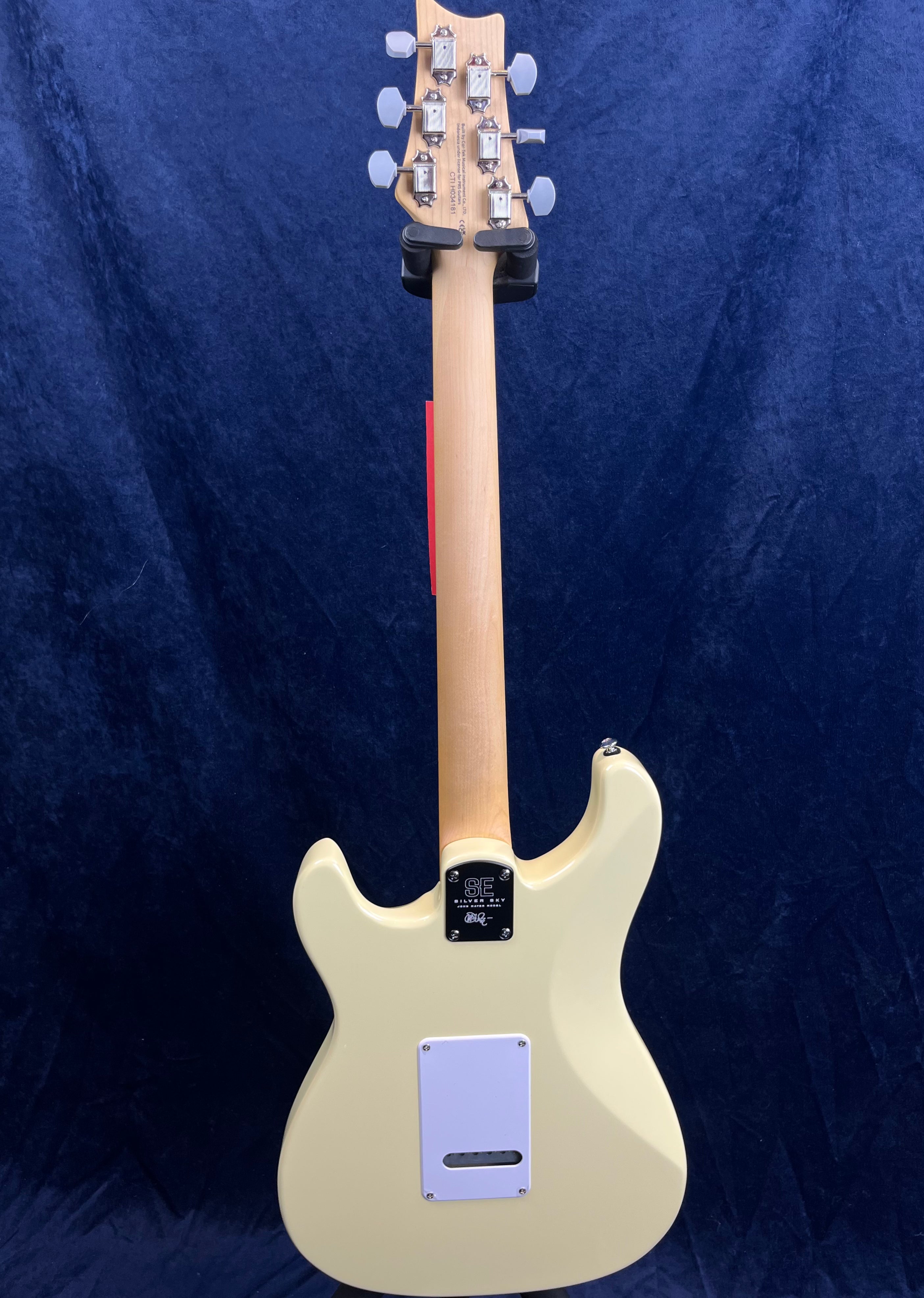 Cream-colored electric guitar shown from the back, with a natural wood neck, white backplate, and silver tuning pegs against a dark blue background.