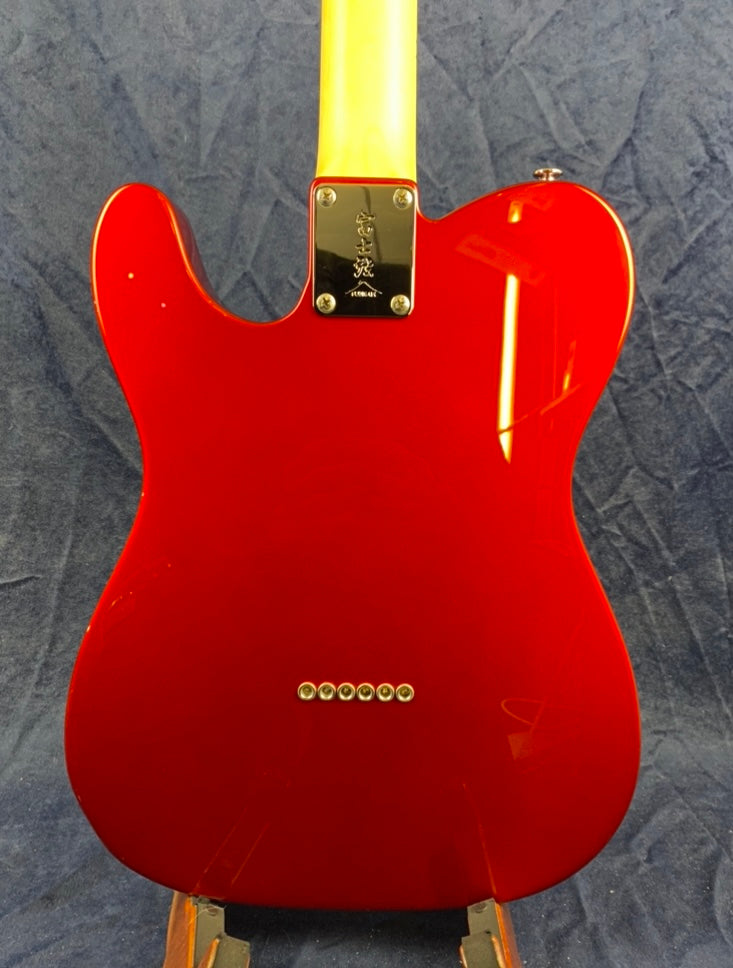 Bright red electric guitar body with a yellow neck, six string holes, and a metal neck plate engraved with symbols.