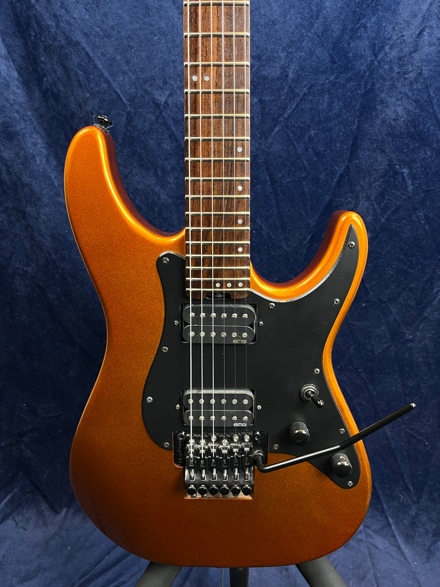 Metallic orange electric guitar with black pickguard, two humbucker pickups, Floyd Rose bridge, whammy bar, and rosewood fretboard.