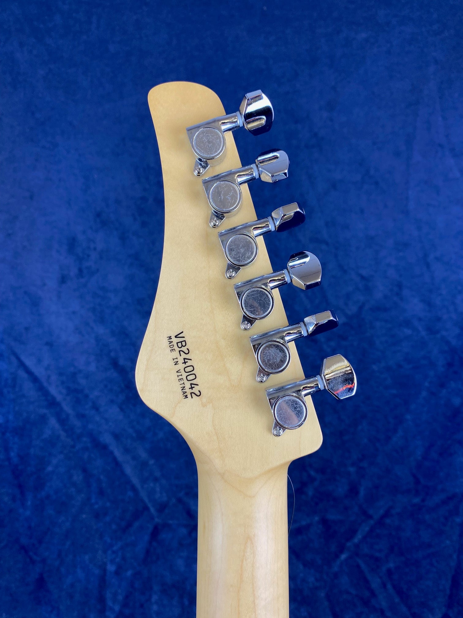 Back of an electric guitar headstock with six chrome tuning pegs and serial number VB240642 stamped above "Made in Vietnam" on natural wood.