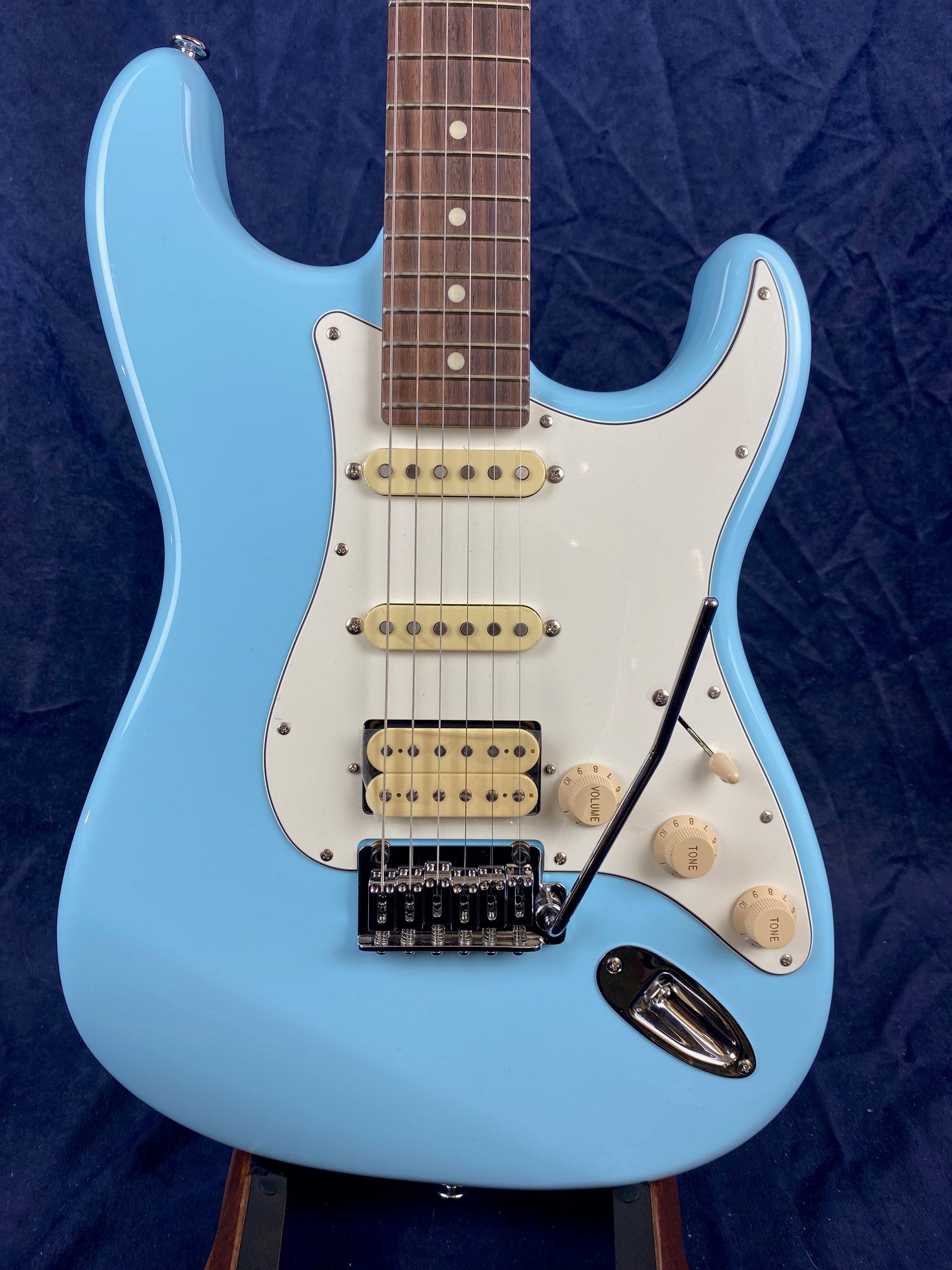 Light blue electric guitar with three cream pickups, white pickguard, three control knobs, tremolo arm, and a rosewood fretboard.
