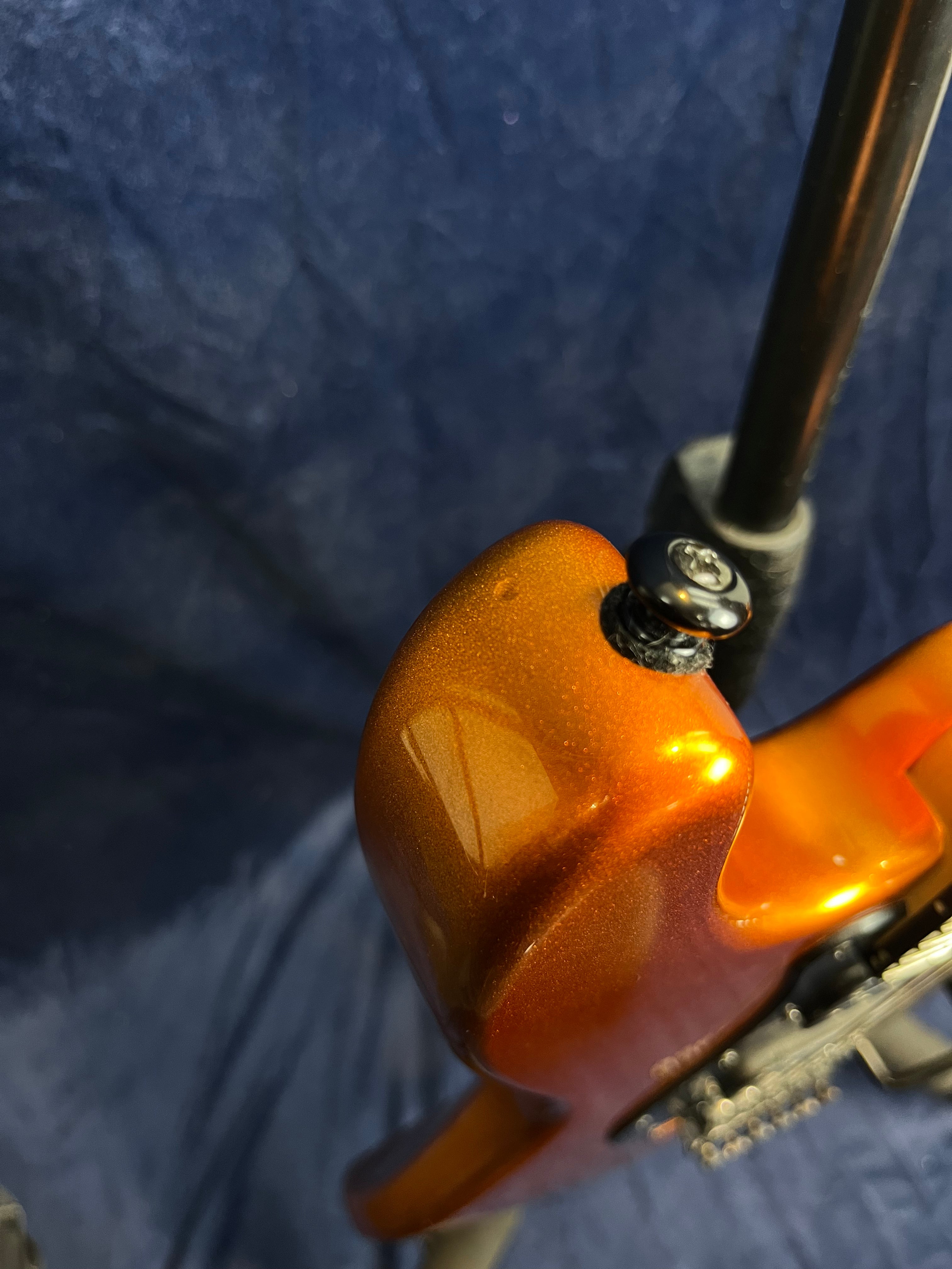 Close-up of a metallic orange electric guitar body showing the strap button and contour near the neck joint.