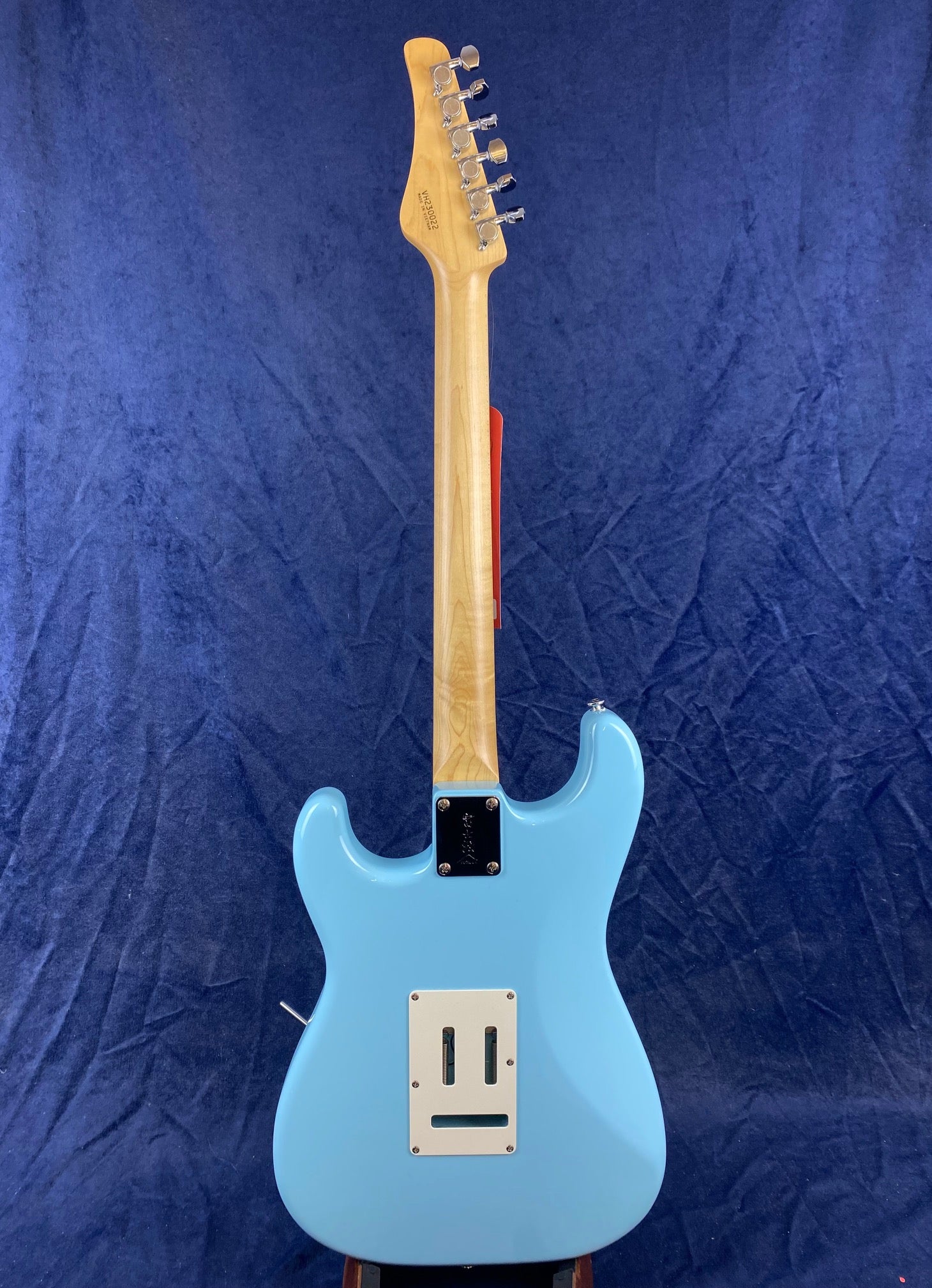 Light blue electric guitar shown from the back, with a natural wood neck and a white rectangular plate near the bottom.
