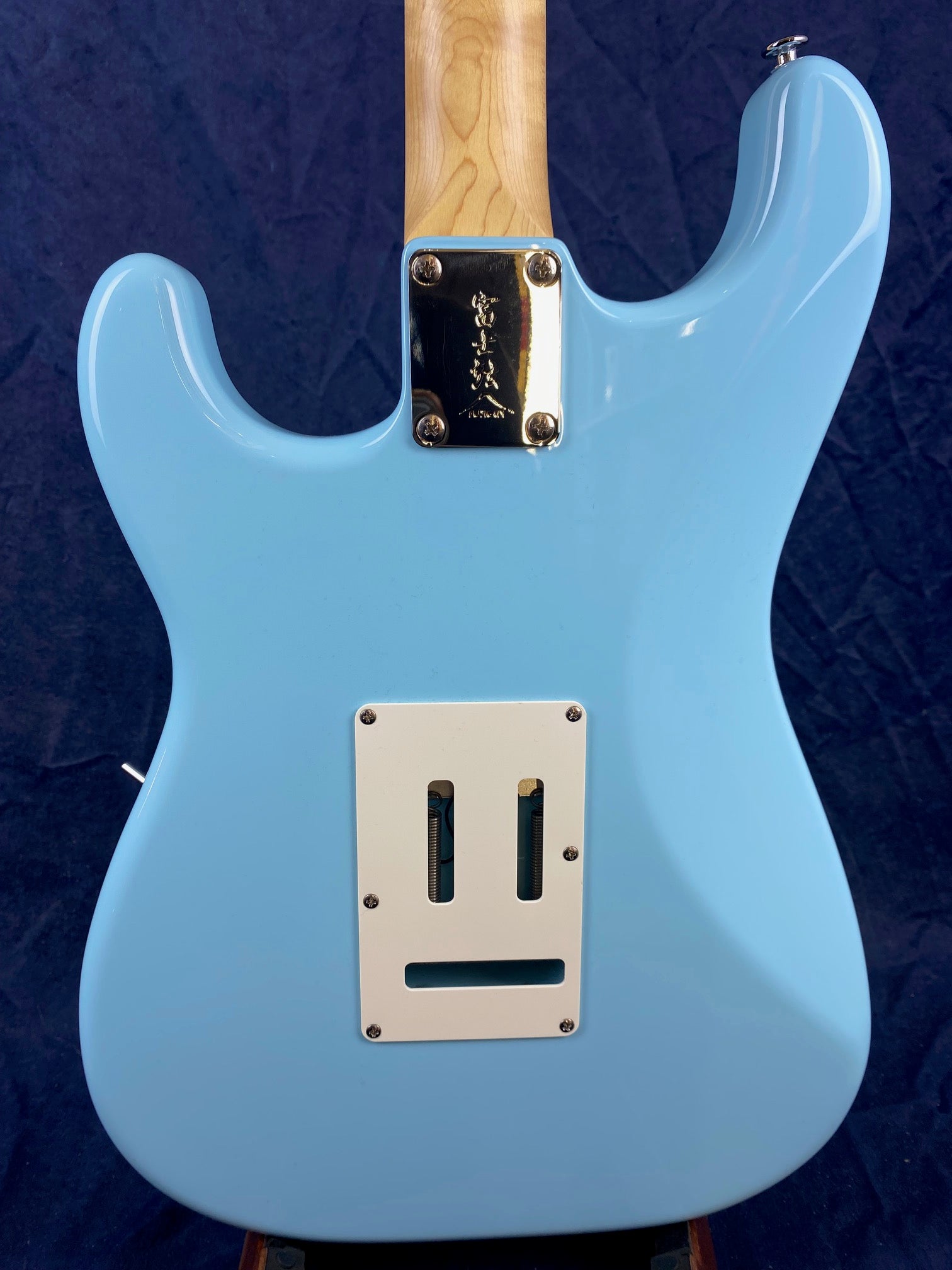 Light blue electric guitar back, white rectangular cover for tremolo springs, chrome neck plate with engraving, natural wood neck.